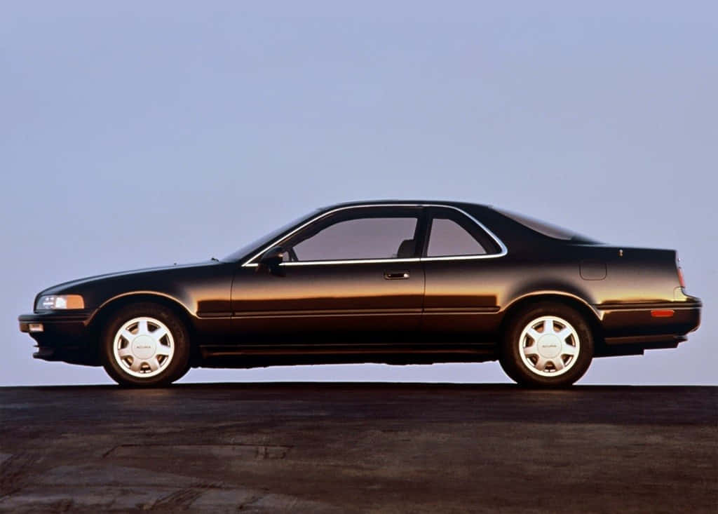 Acura Legend 桌布 壁紙 — 一輛時尚的黑色轎跑車配銀色輪圈，在深色路面上以側面輪廓襯托著清澈的藍天。