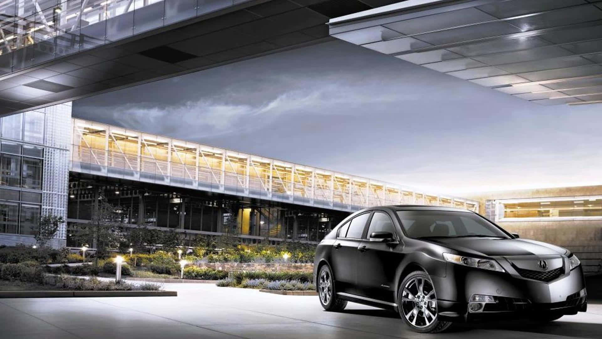Acura Tl 桌布 壁紙 — 一輛時尚的黑色轎車停放在現代玻璃和鋼製簷篷下，周圍有照明步道和景觀花園，正值黃昏。