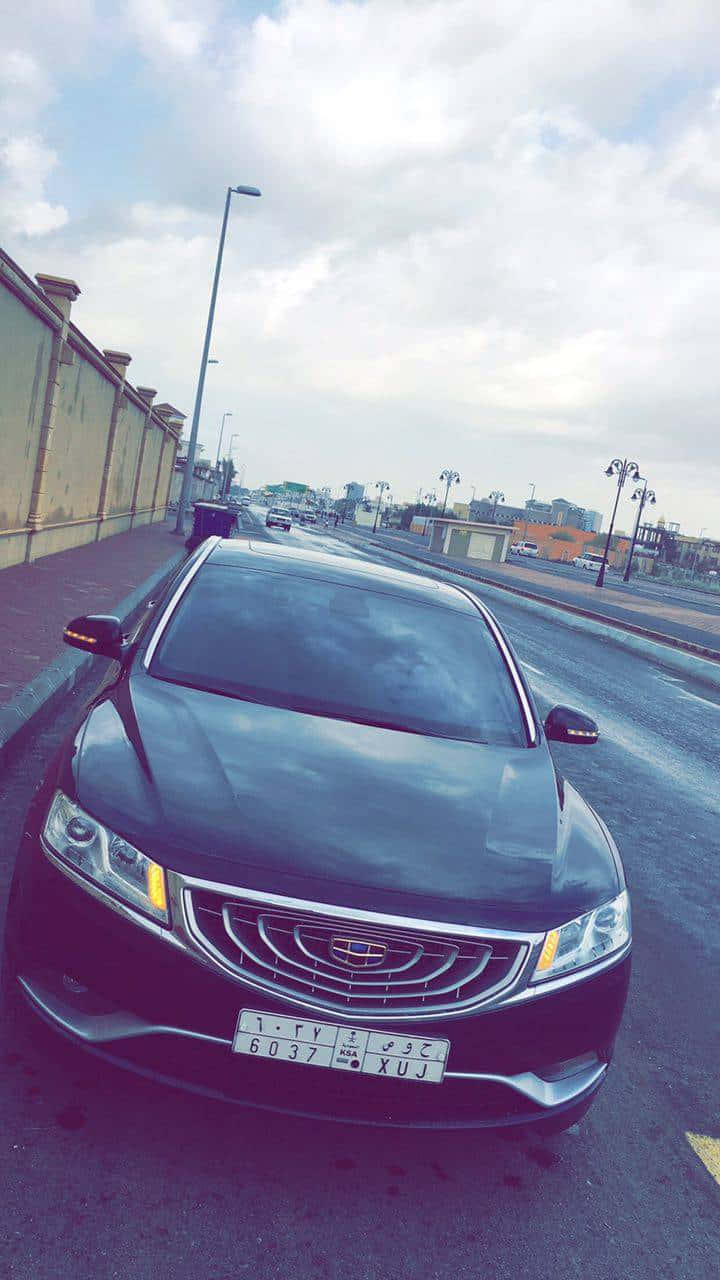 Geely 桌布 壁紙 — 一輛時尚的黑色轎車停泊在潮濕的城市街道上，背景是陰天、街燈和建築物。