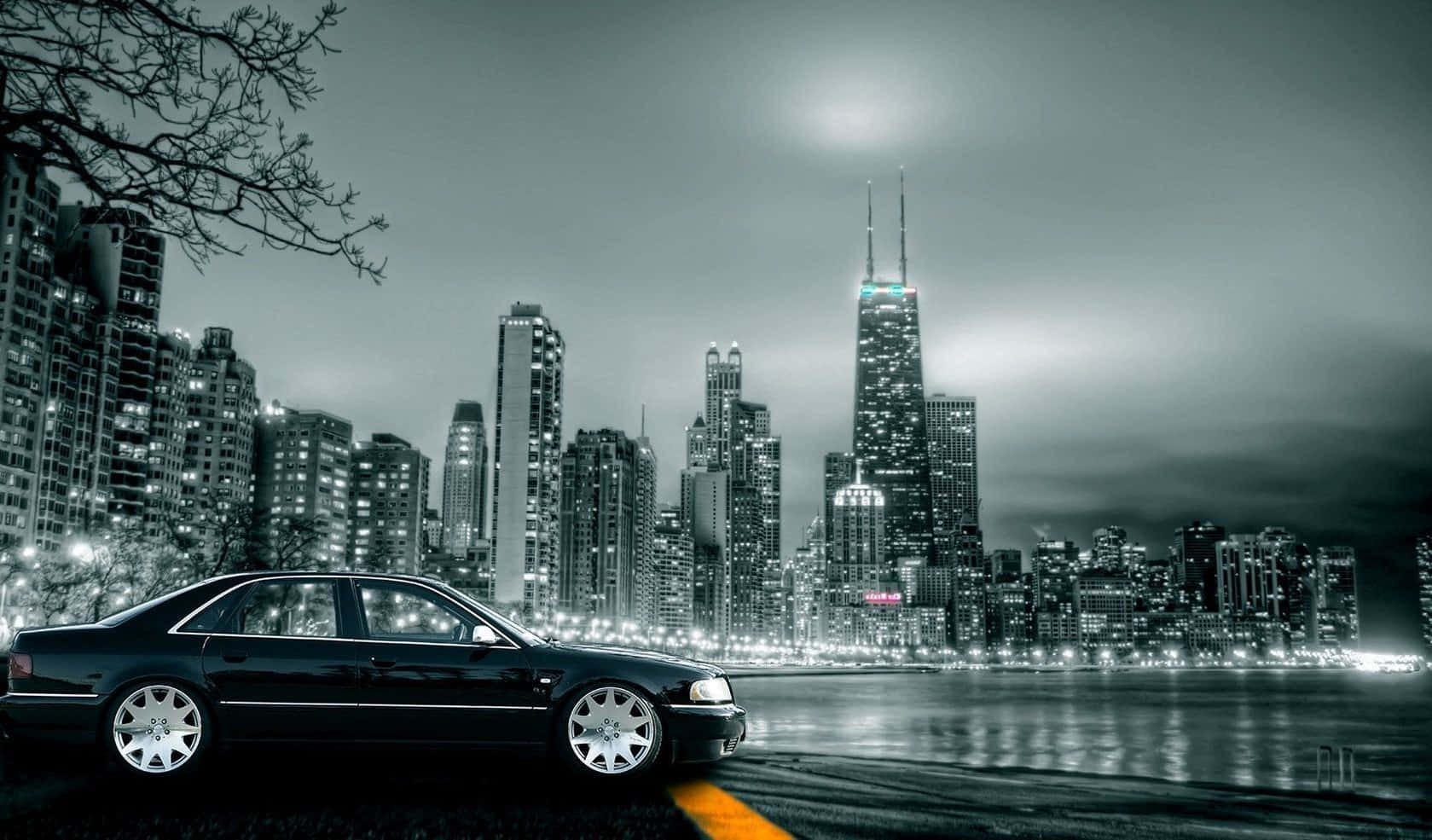 Black And White Cityscape 桌布 壁紙 — 一輛時尚的黑色轎車在黃昏時停泊在河邊，背景是閃爍的城市天際線。