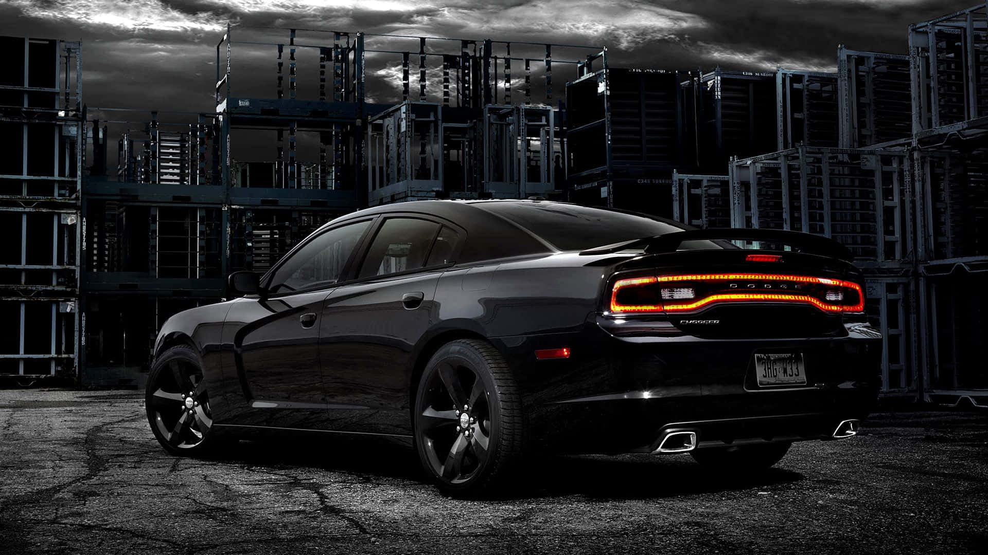 Dodge Charger 桌布 壁紙 — 一輛時尚的黑色道奇Charger，帶有發光的橙色尾燈，停放在風暴天空下粗糙的工業場地中。