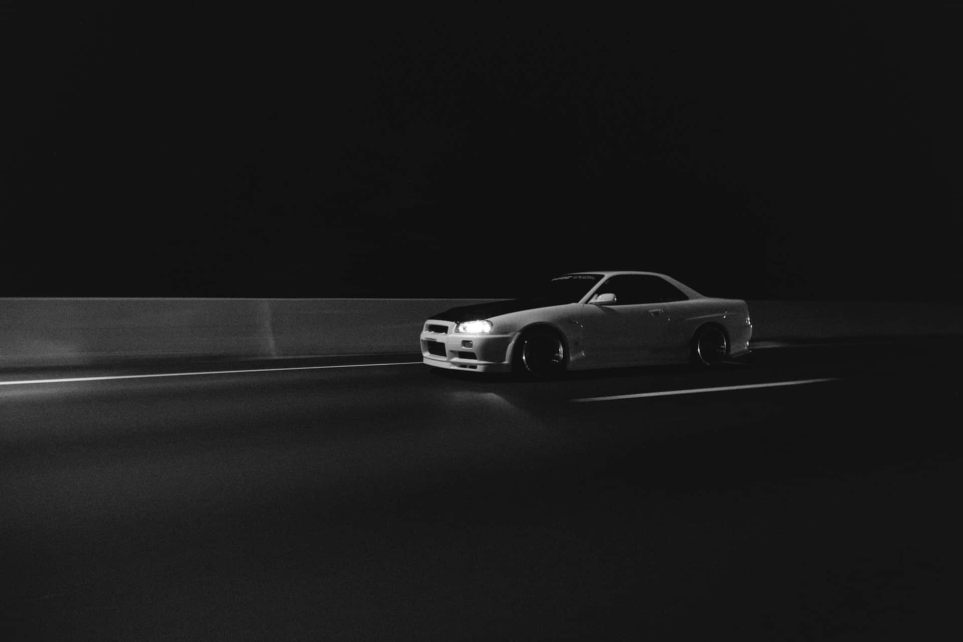 Black And White Car 桌布 壁紙 — 一輛時尚跑車在夜間獨自行駛在黑暗的高速公路上，車頭燈劃破黑暗。