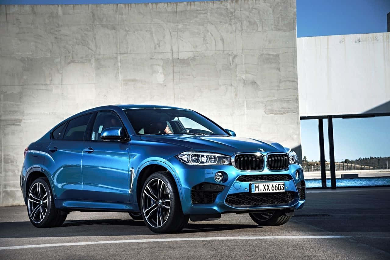 Bmw X6 桌布 壁紙 — 一輛時尚金屬藍色BMW X6 M在明亮日光下停泊在簡約混凝土牆旁。