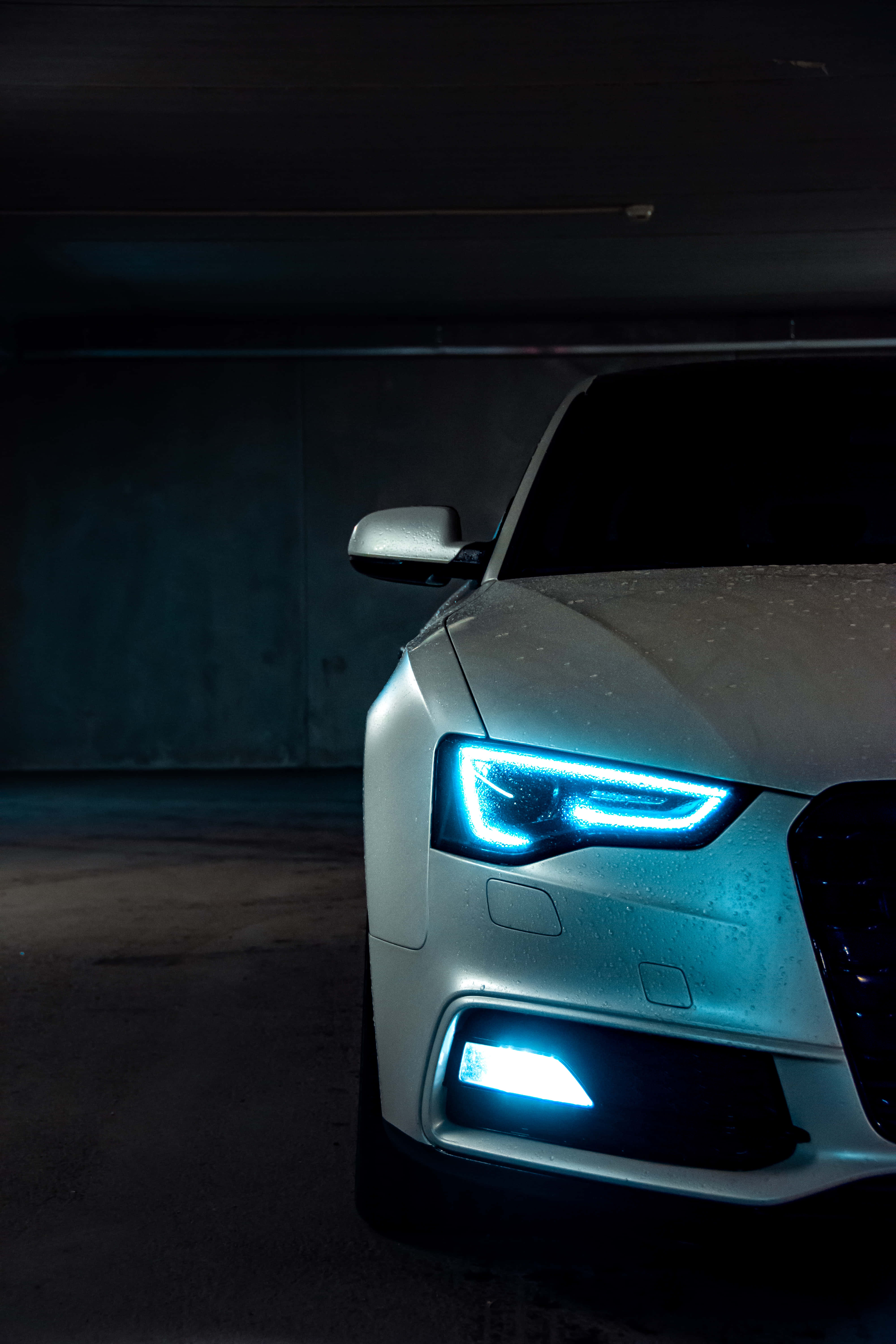 Best Car 桌布 壁紙 — 一輛時尚銀色汽車的發光藍色車頭燈刺穿了地下停車場的黑暗。