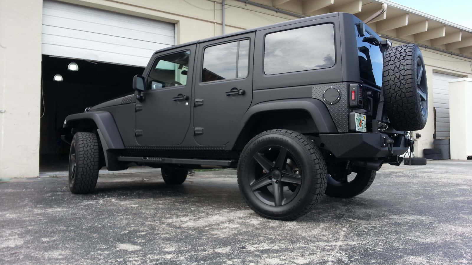 啞光黑色Jeep Wrangler停泊在混凝土場地上的車庫前。