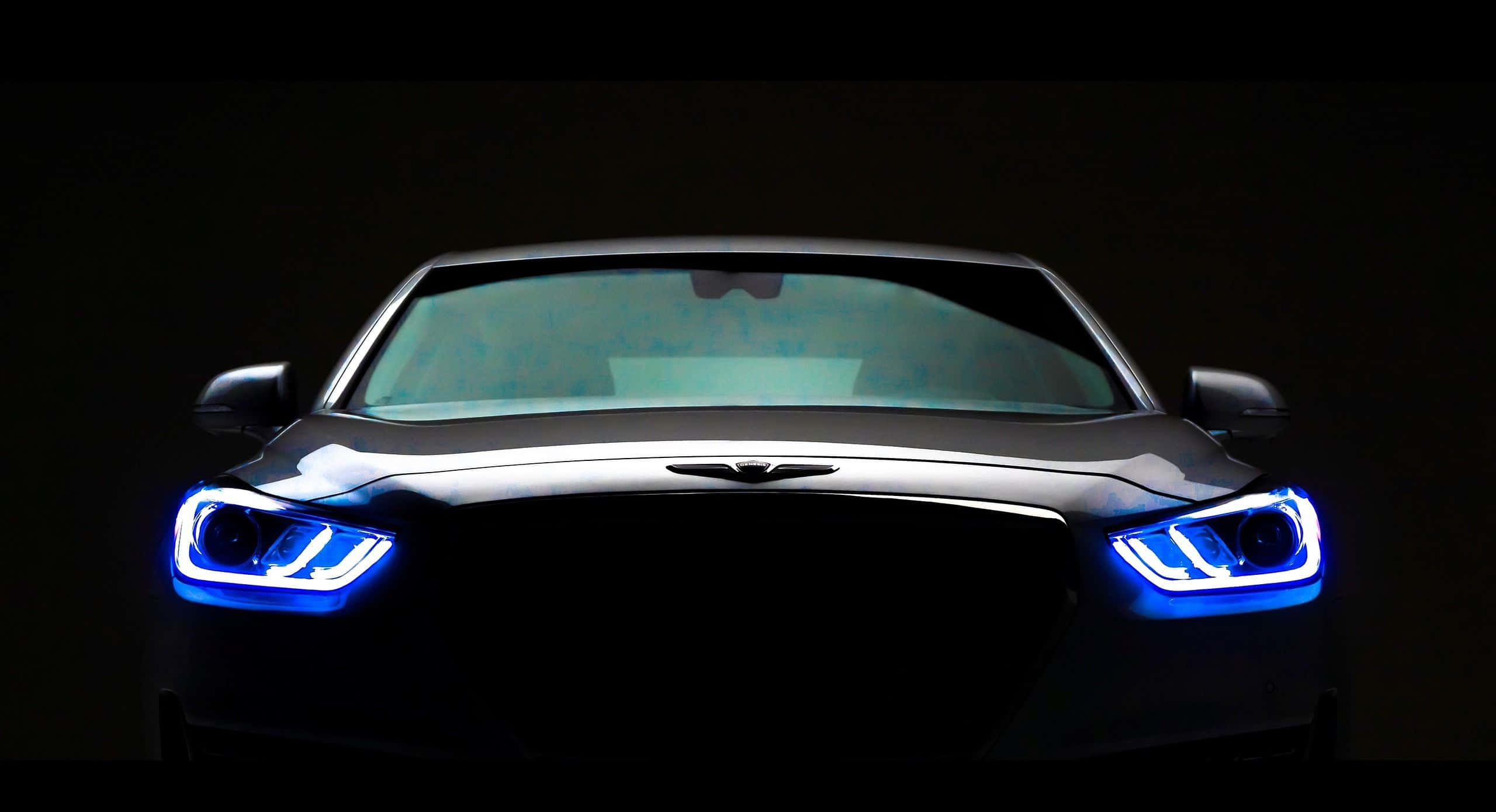 Genesis G90 桌布 壁紙 — 一輛時尚黑色汽車的正面視圖，在黑暗背景下被鮮豔的藍色車頭燈照亮。