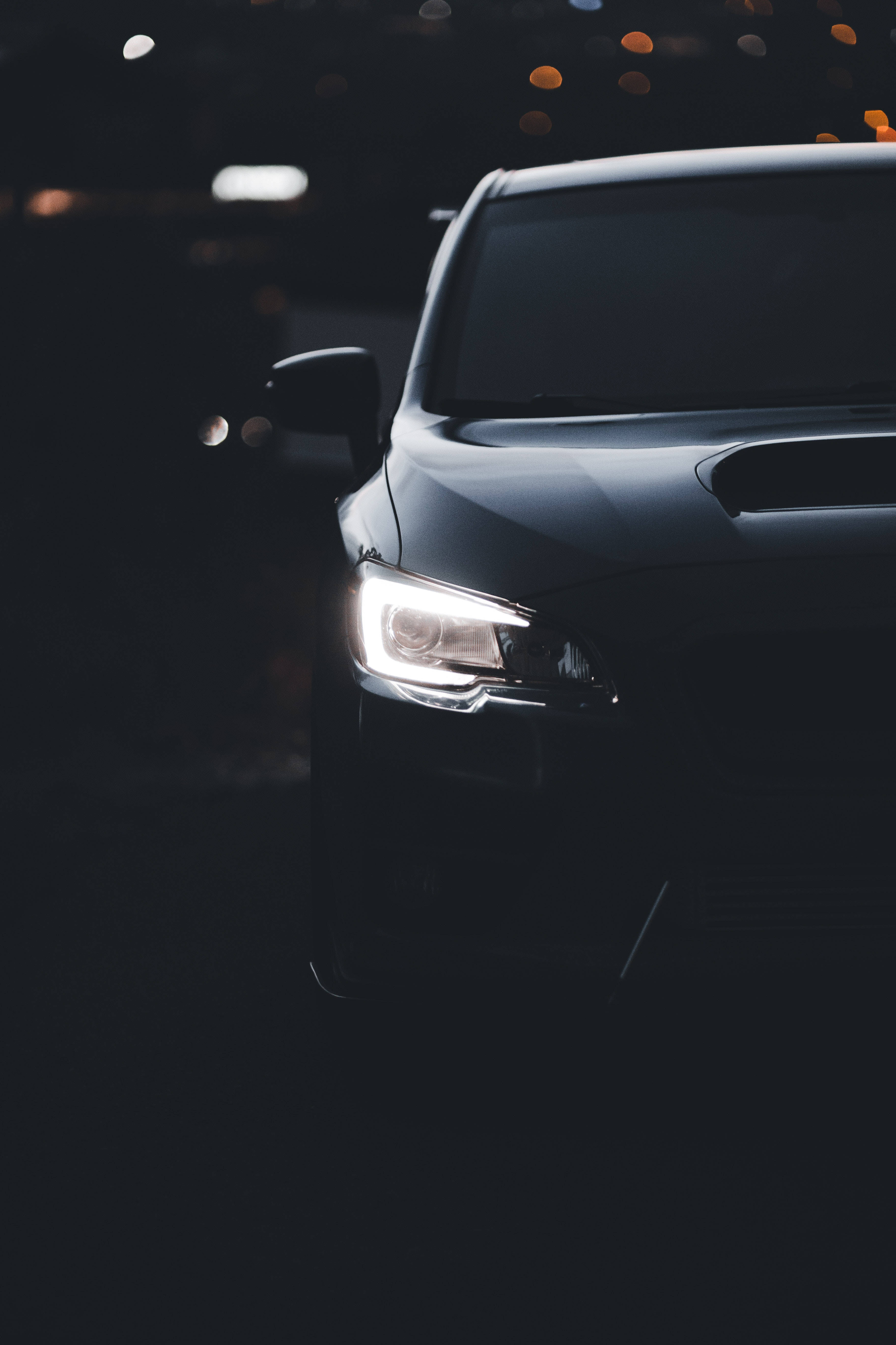 4K 桌布 壁紙 — 一輛時尚黑色汽車的發光車頭燈，在背景的散景燈光中劃破黑暗。
