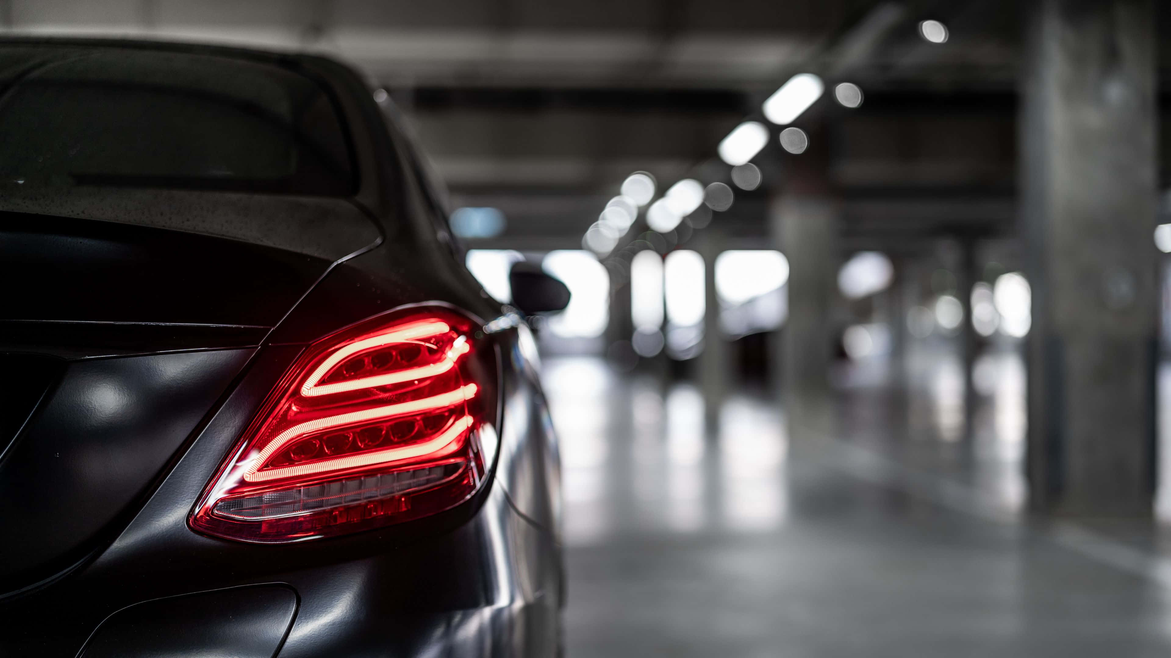 4K Mercedes 桌布 壁紙 — 一輛時尚黑色汽車的紅色尾燈在光線昏暗的地下停車場中格外醒目。