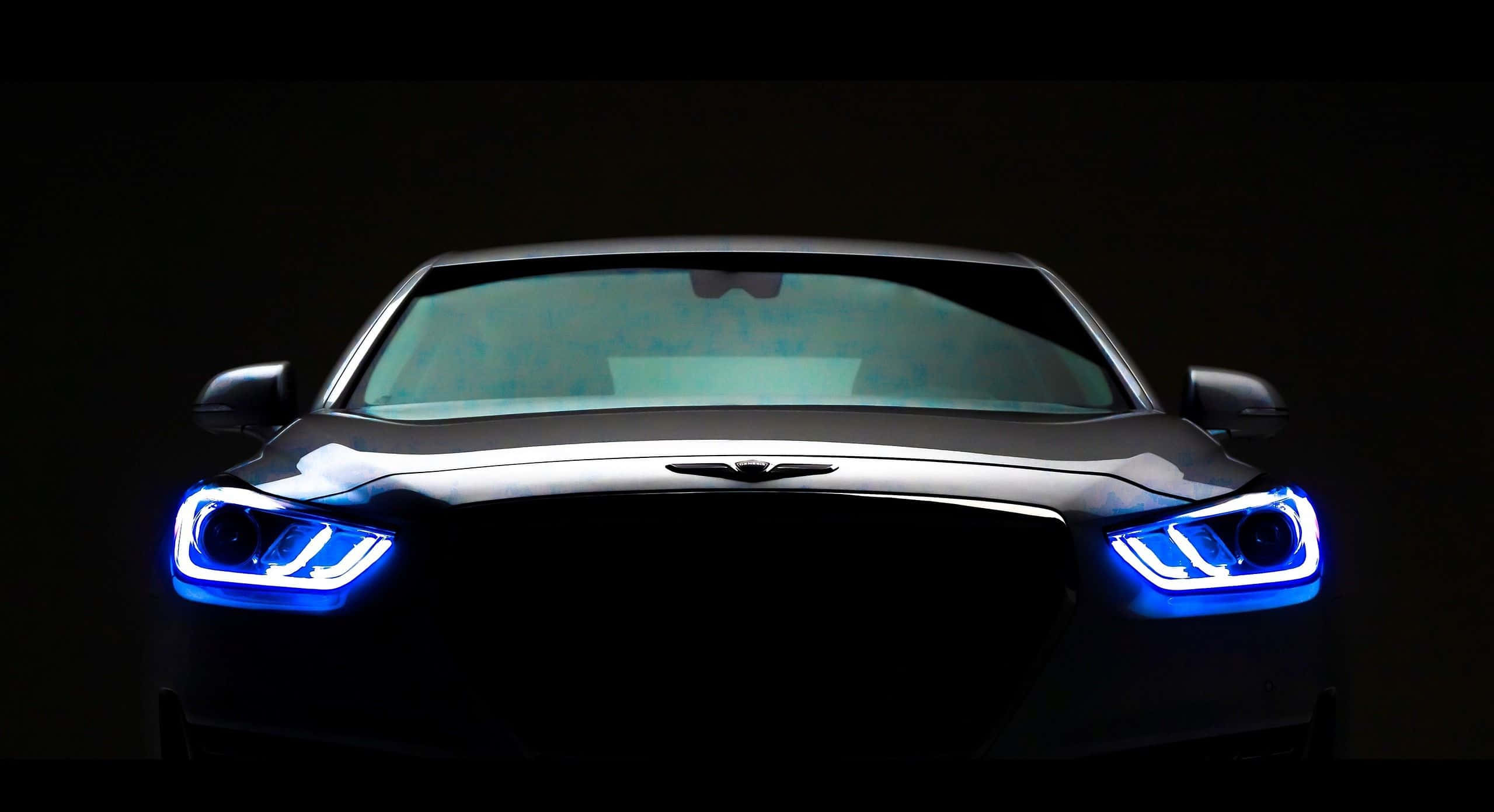 Hyundai Genesis 桌布 壁紙 — 一輛時尚黑色跑車的發光藍色頭燈在戲劇性的工作室拍攝中刺穿黑暗。