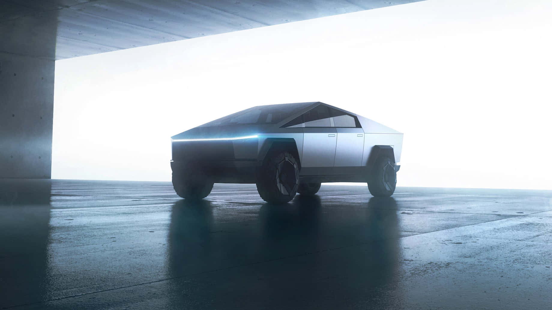 tesla 桌布 壁紙 — 一輛未來感十足的銀色Cybertruck停在混凝土天橋下，藍色發光車頭燈在潮濕的路面上反射。