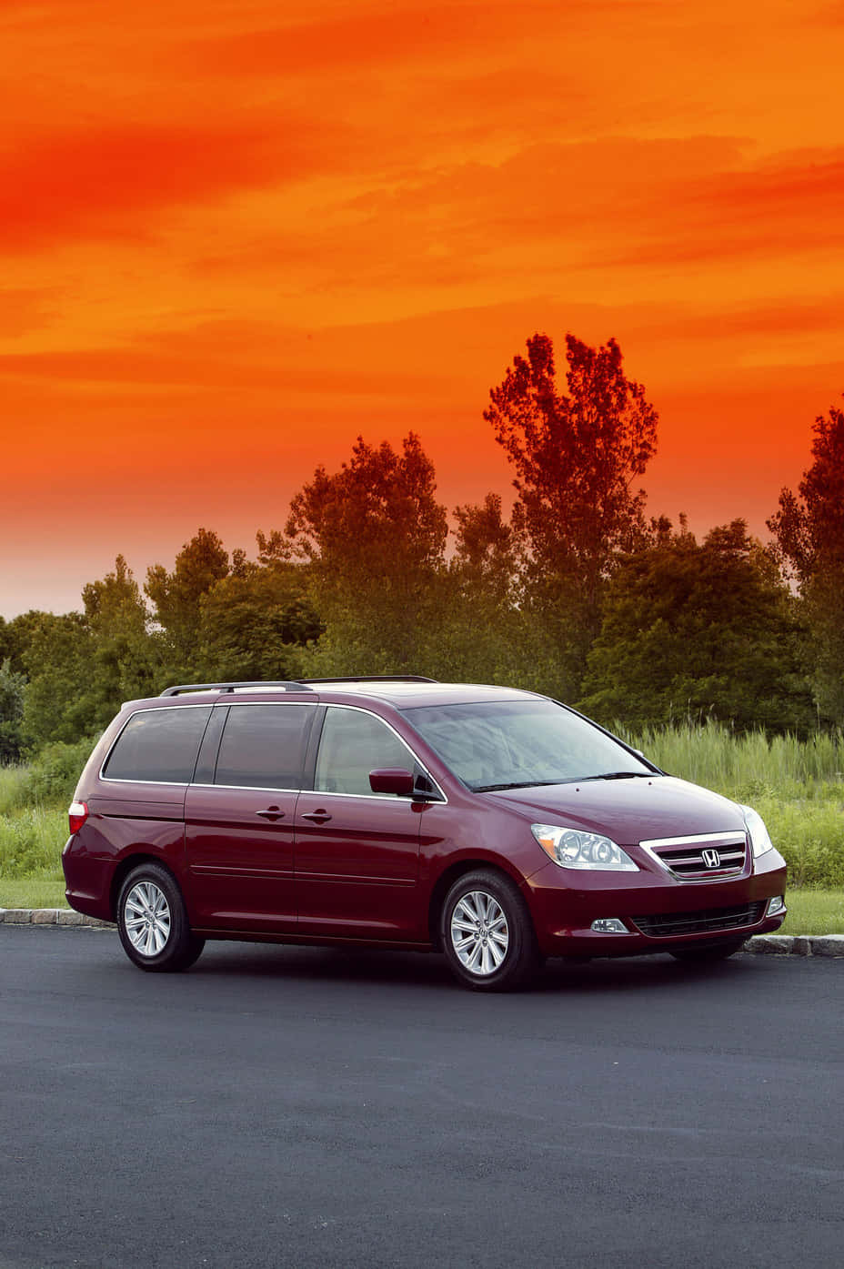 Honda Odyssey 桌布 壁紙 — 一輛栗色小型貨車停在瀝青路上，背景是火紅的橙色日落天空和剪影樹木。