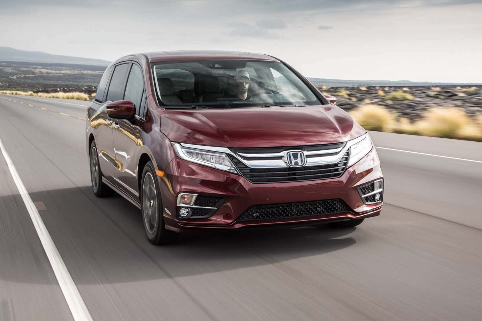 Honda Odyssey 桌布 壁紙 — 一輛栗色本田小型貨車在沙漠高速公路上飛馳，周圍環境模糊，遠山在陰天天空下。