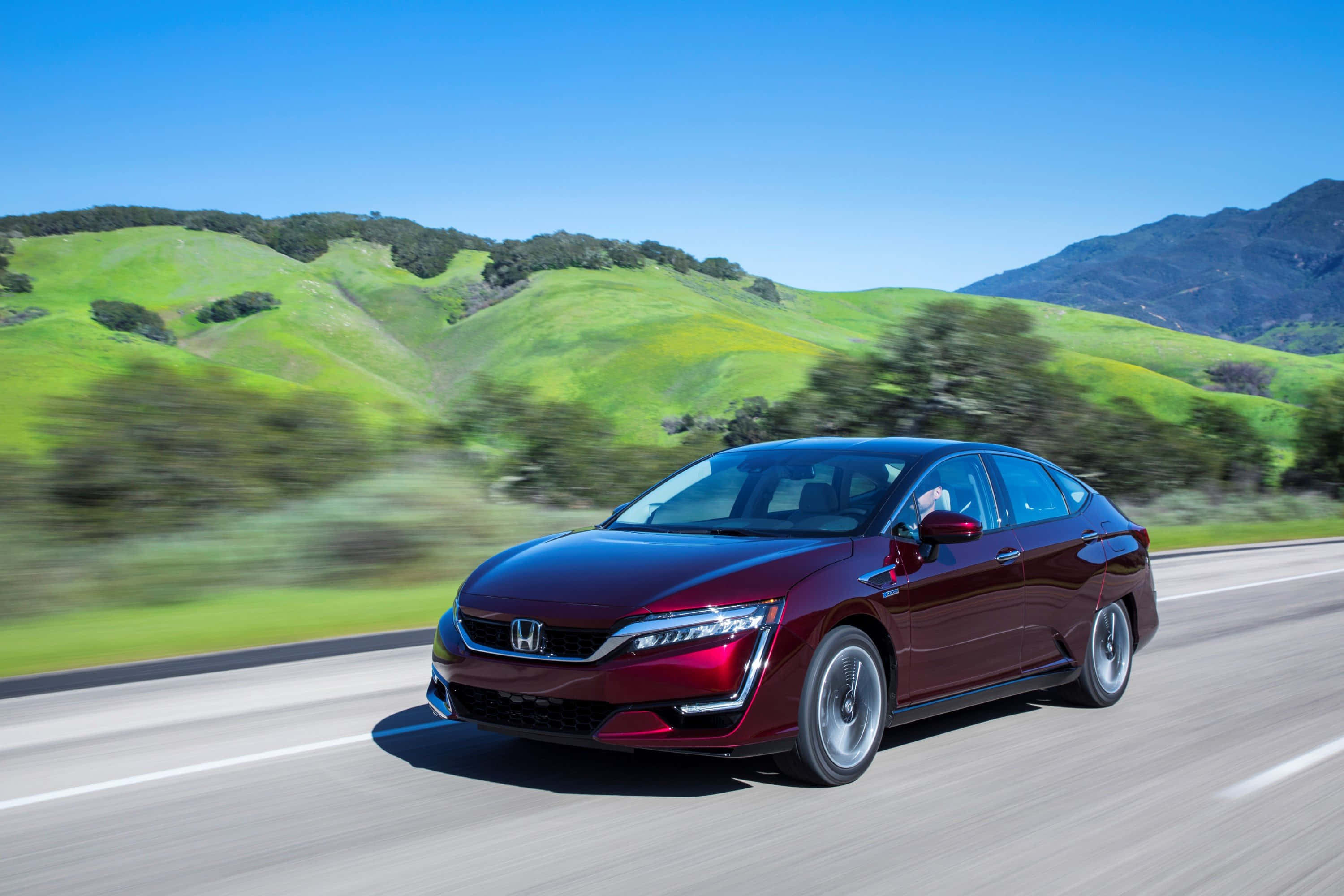 Honda Clarity 桌布 壁紙 — 一輛栗色本田轎車在陽光明媚的高速公路上疾馳，背景是模糊的綠色山丘和藍天。