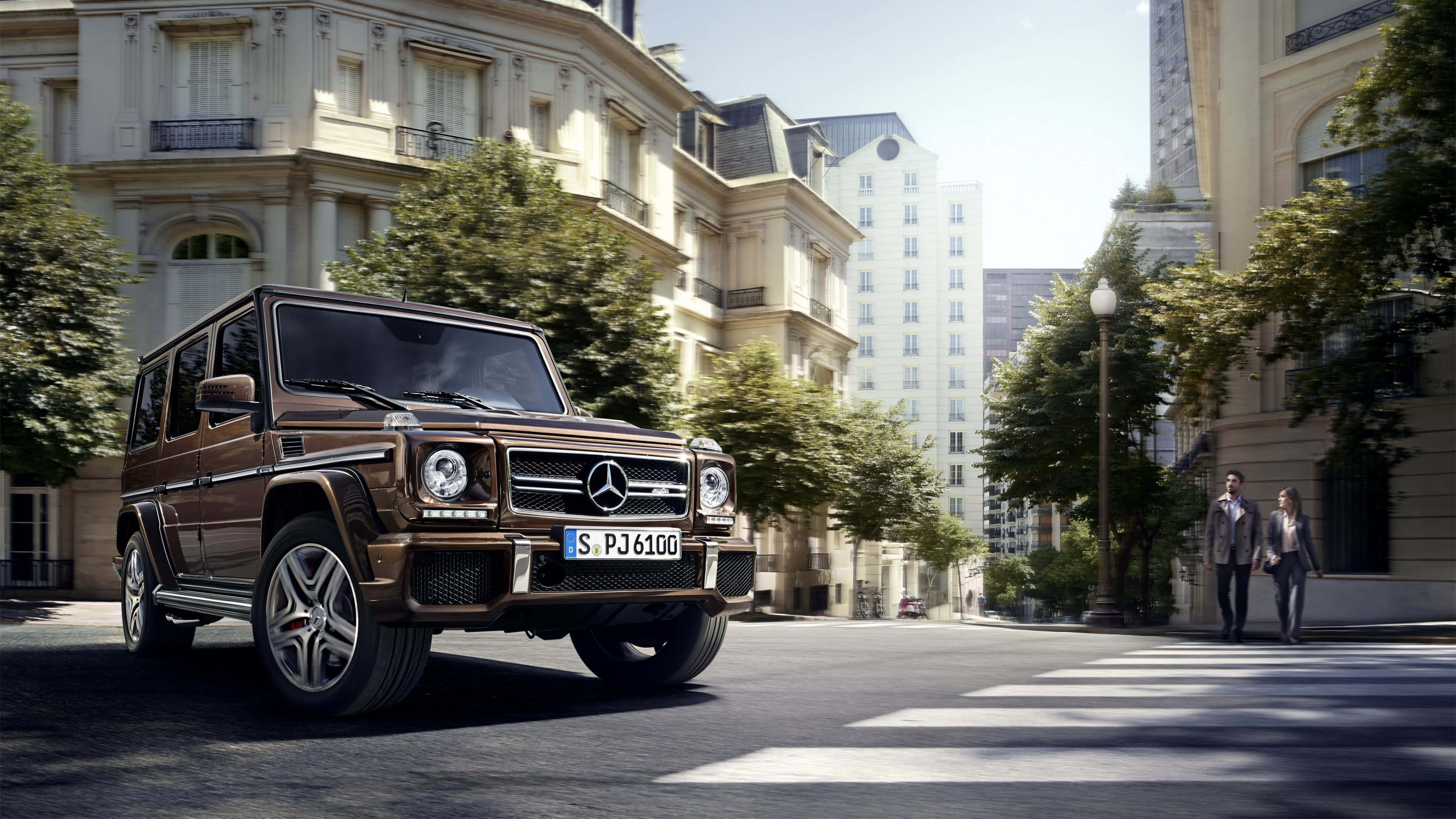 4K Mercedes 桌布 壁紙 — 一輛棕色 Mercedes G-Class SUV 在明亮的日光下行駛在巴黎一條綠樹成蔭的街道上，有行人和經典建築。