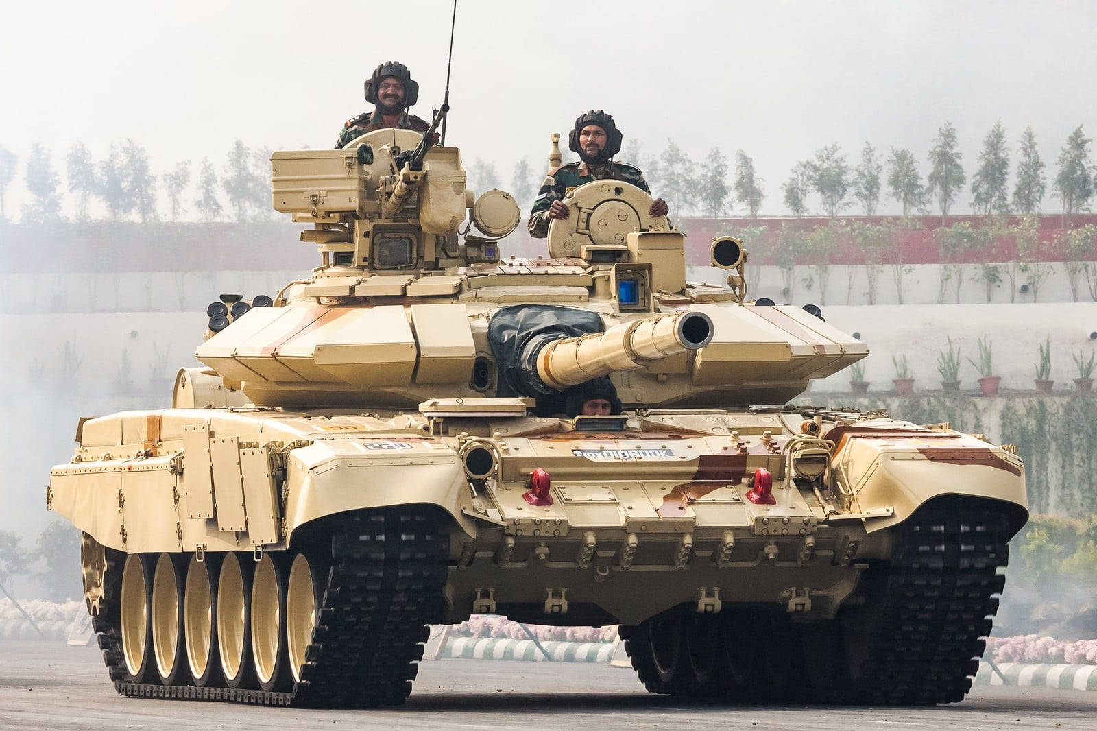Indian Army 桌布 壁紙 — 一輛棕褐色裝甲坦克，頂部有士兵，在鋪砌的軌道上向前移動，身後留下煙霧。