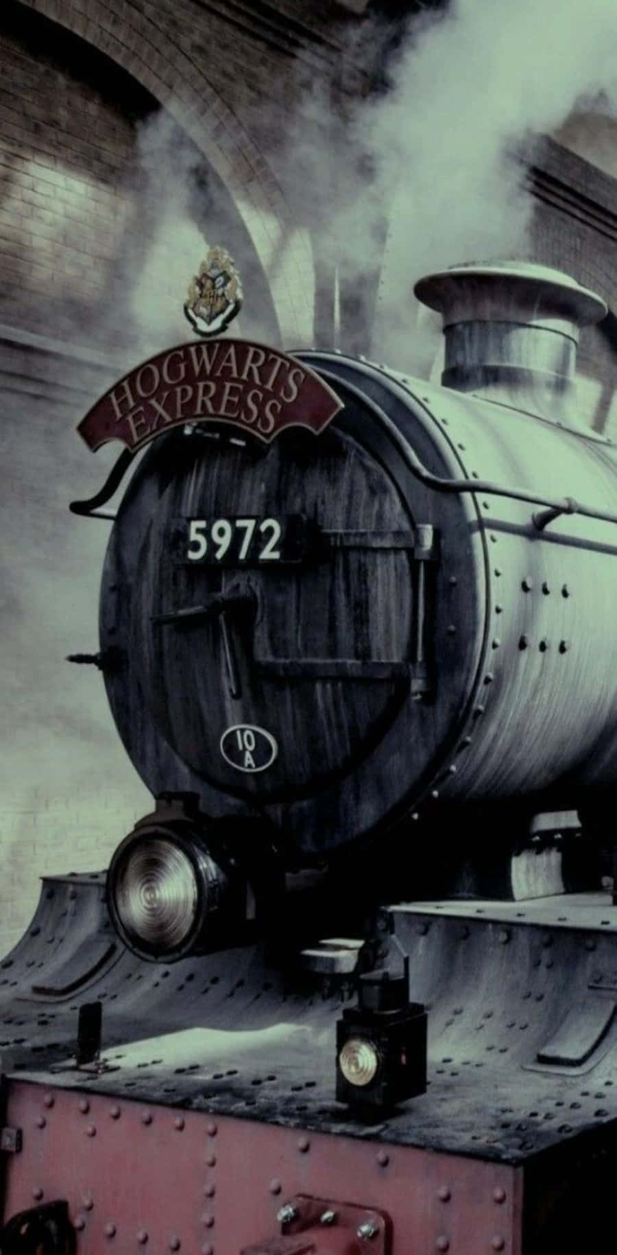 The Hogwarts Express Train 桌布 壁紙 — 一輛標有霍格華茲特快車的雄偉蒸汽火車頭，在煙霧瀰漫的車站石拱門下噴出煙霧。