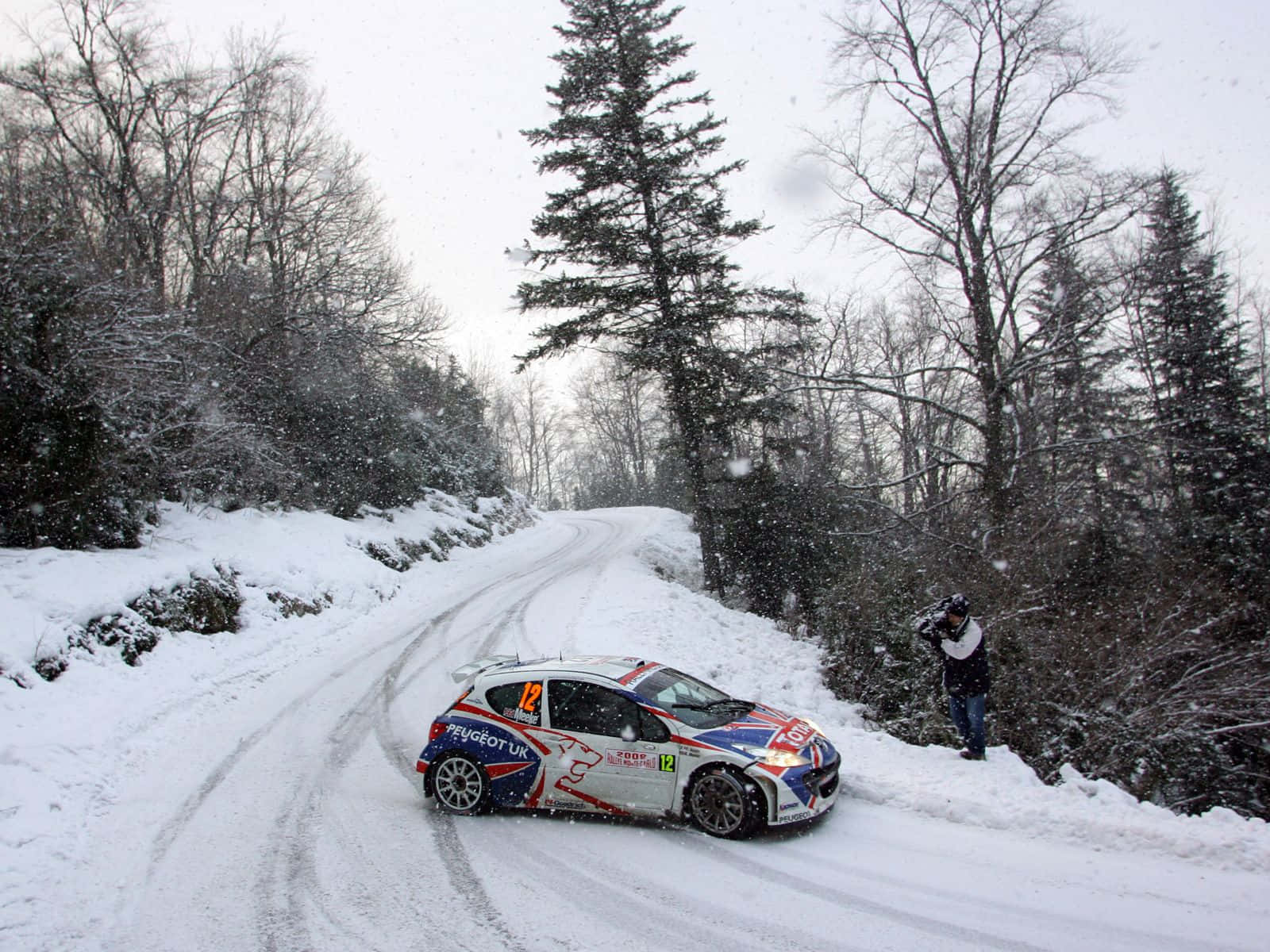 Ice Racing 桌布 壁紙 — 一輛標緻拉力賽車在雪花飄落的雪地森林道路上飛馳，攝影師捕捉了這一刻。