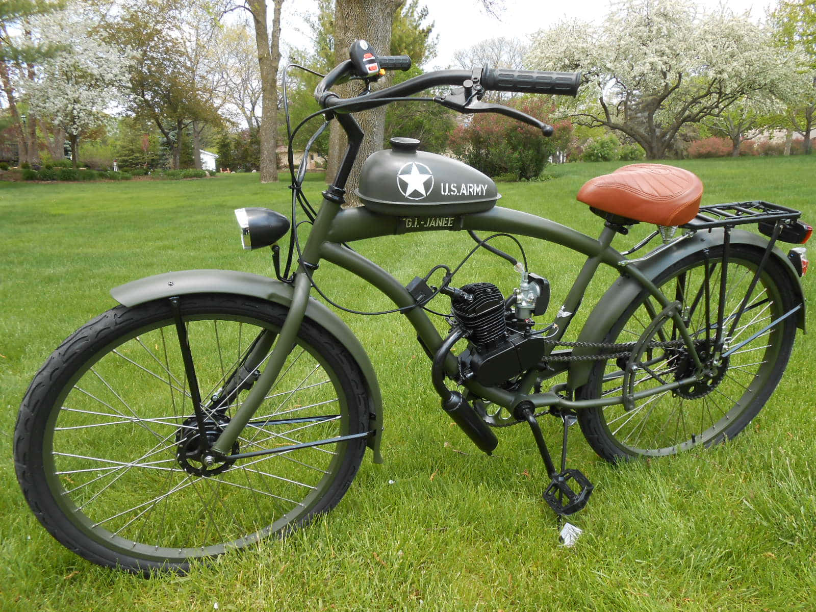 Bicycle 桌布 壁紙 — 一輛橄欖綠軍用風格單車，帶有美國陸軍油箱和橙色座椅，停放在有開花樹木的草地上。