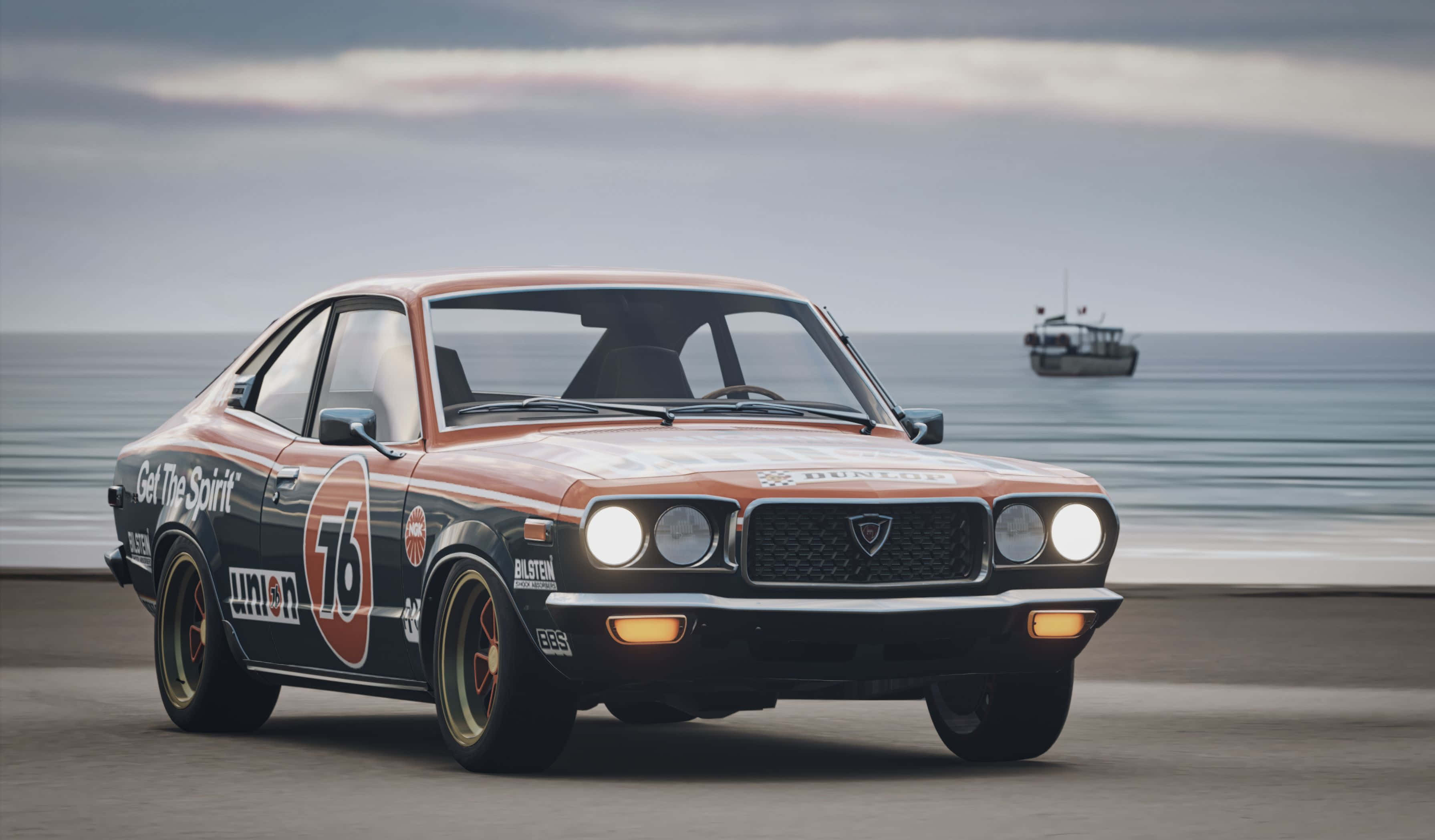 Mazda Rx-3 桌布 壁紙 — 一輛橙色和黑色塗裝的復古賽車沿著海岸公路飛馳，在陰天天空下，地平線上可見一艘船。