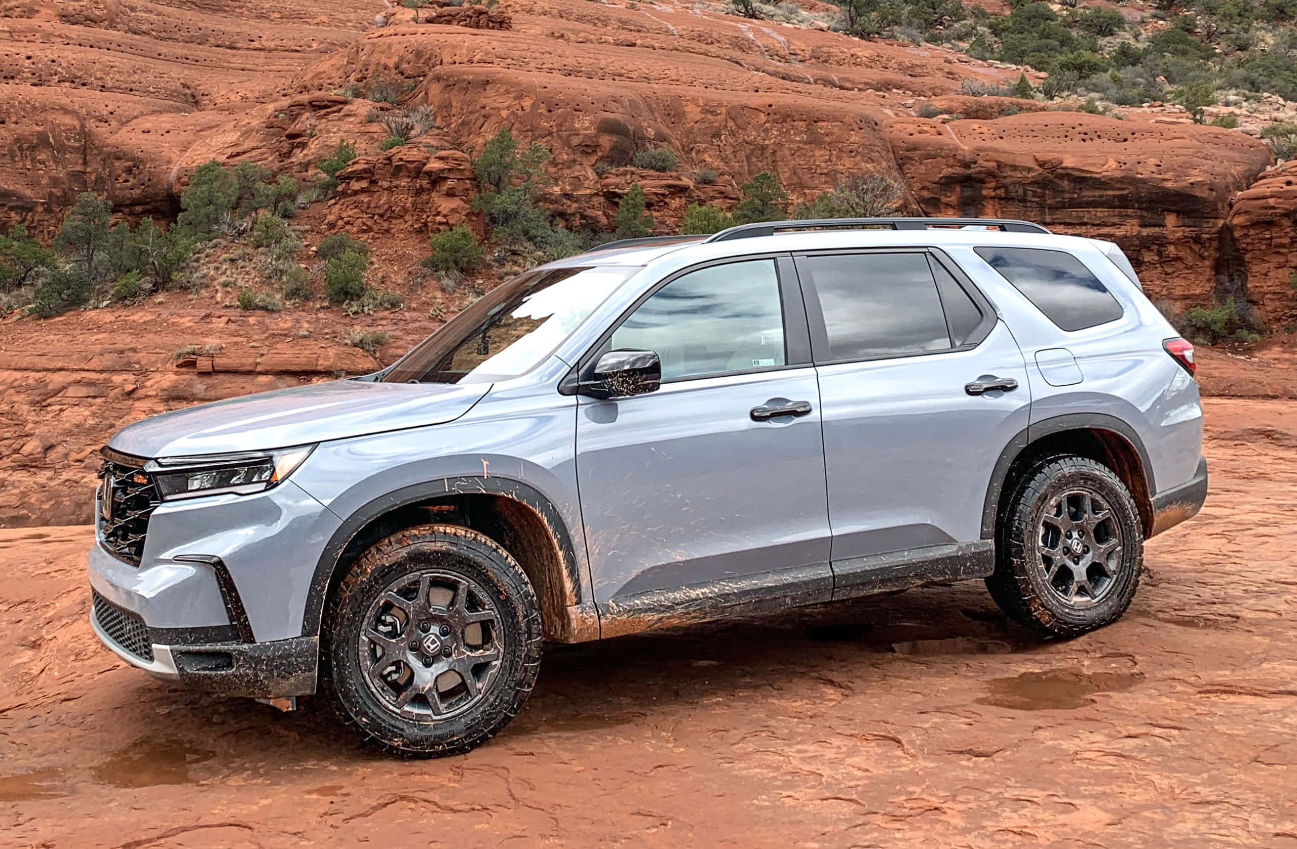 Honda Pilot 桌布 壁紙 — 一輛沾滿泥巴的銀色SUV在明亮的日光下行駛於崎嶇的紅色岩石地形。