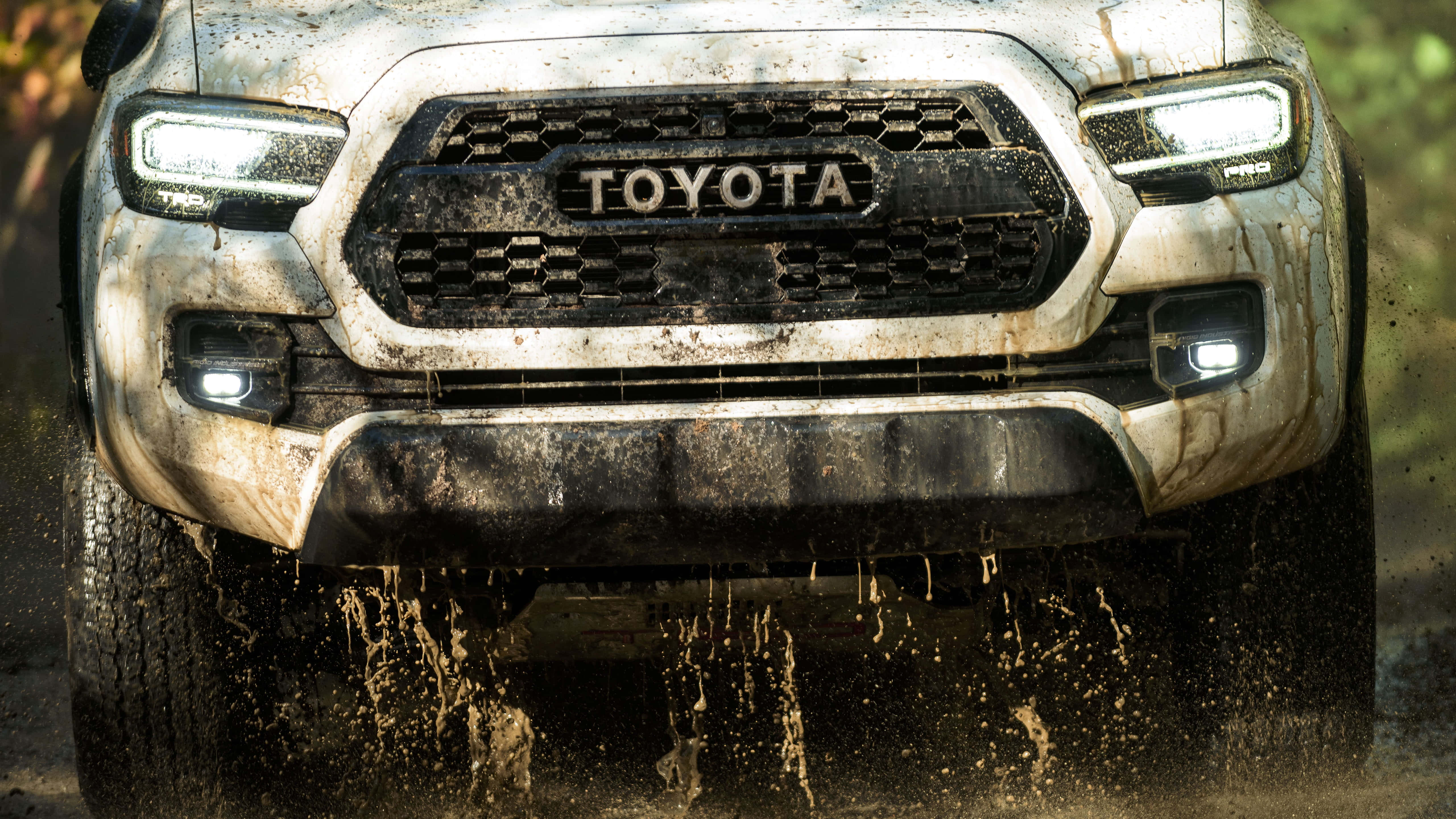 Toyota 桌布 壁紙 — 一輛泥濘的豐田皮卡車在森林小徑上行駛，車頭燈閃爍。