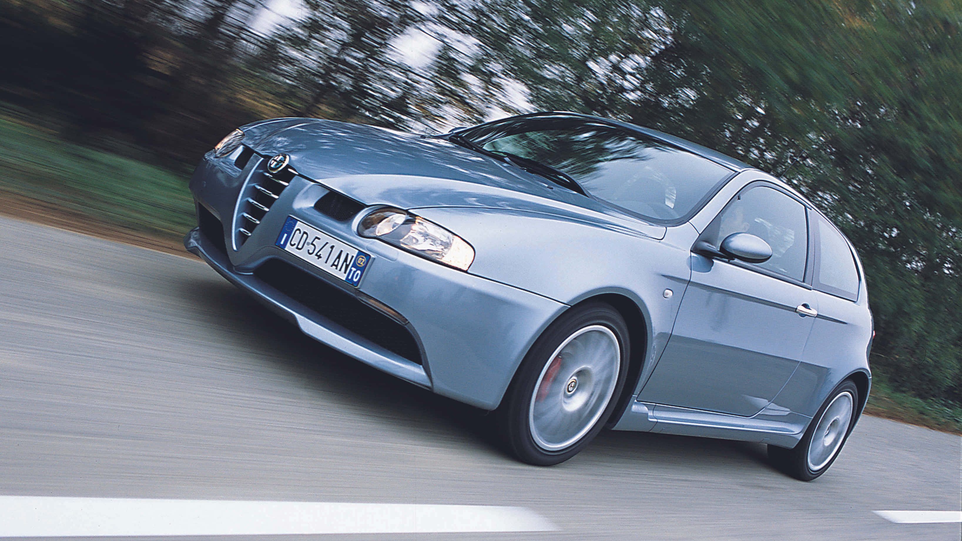 Alfa Romeo Gt 桌布 壁紙 — 一輛流線型的銀色愛快羅密歐跑車在道路上疾馳，背景是模糊的綠色樹木。