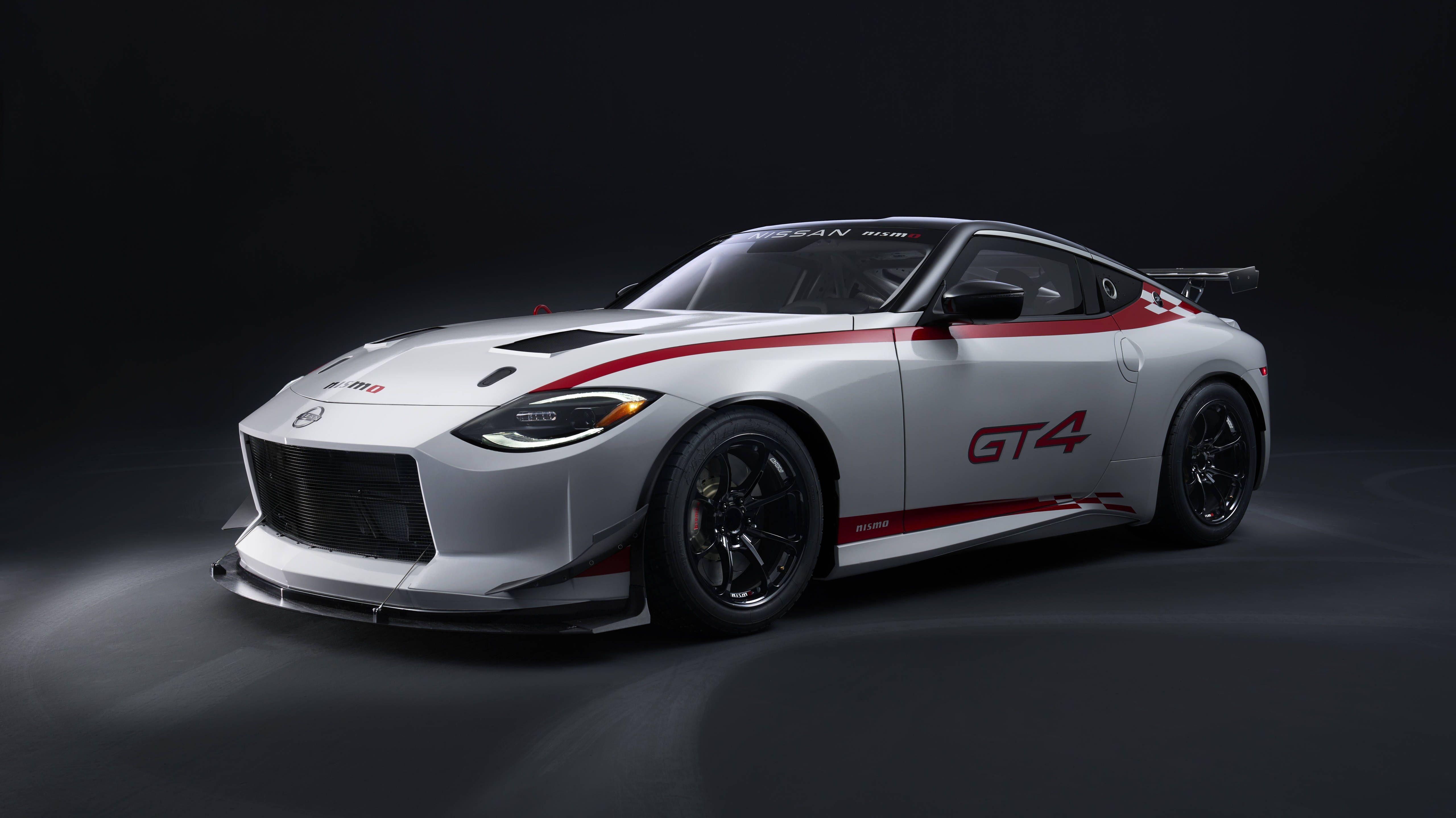 Nissan 桌布 壁紙 — 一輛流線型的銀色日產GT4賽車，帶有紅色點綴和黑色輪圈，在黑暗的攝影棚背景下被戲劇性地照亮。