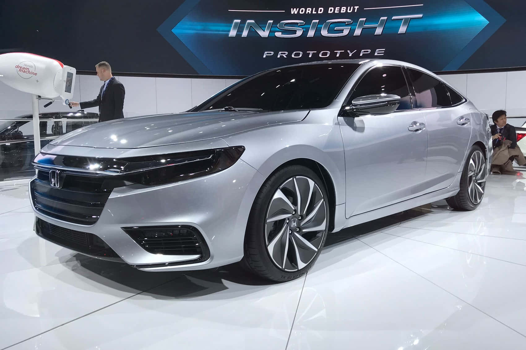Honda Insight 桌布 壁紙 — 一輛流線型的銀色本田Insight原型車在車展的明亮燈光下閃閃發光，背後有一個大型顯示屏幕。