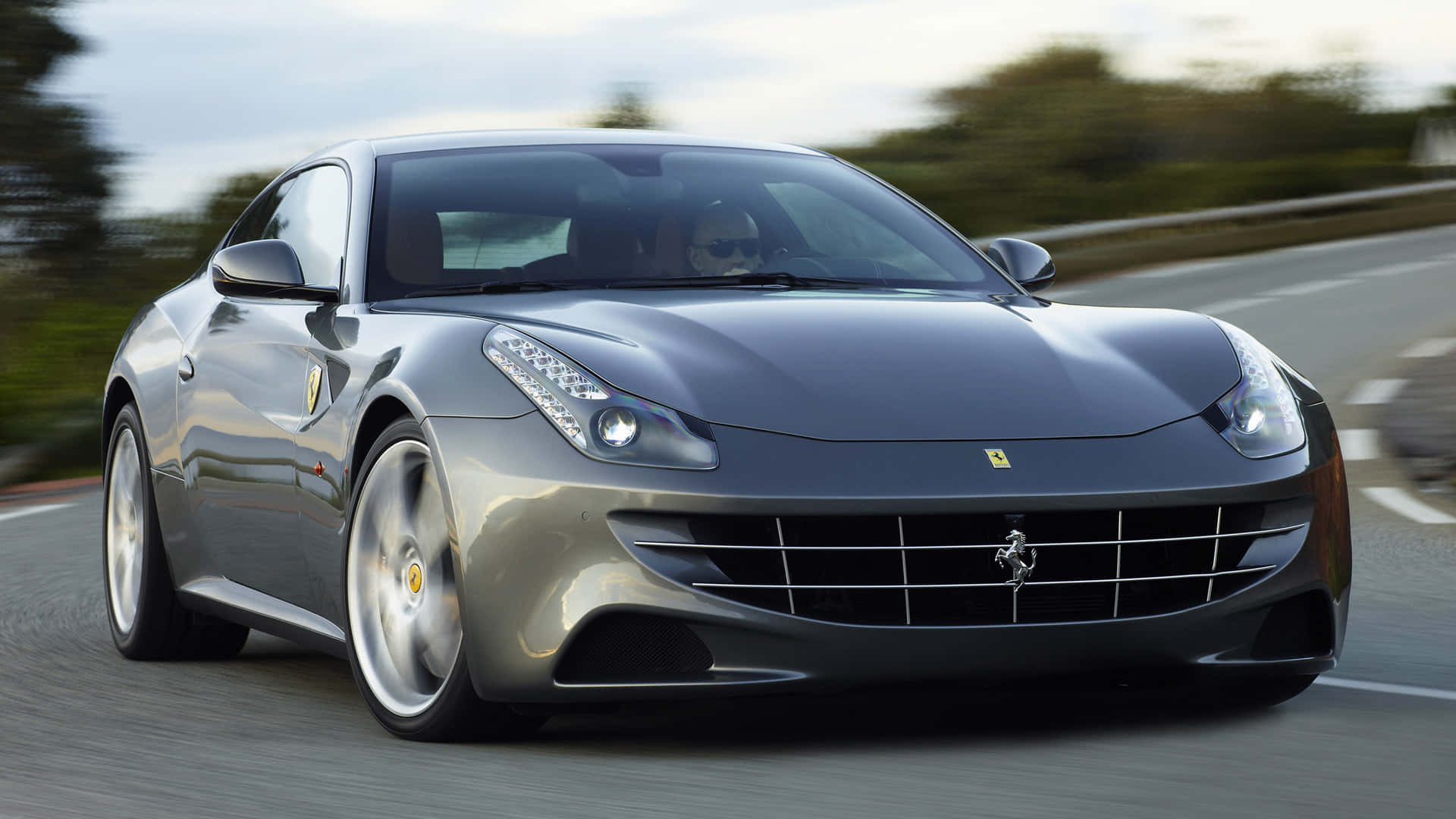 Ferrari Ff 桌布 壁紙 — 一輛流線型的銀色法拉利跑車在蜿蜒的道路上飛馳，背景是模糊的綠意。