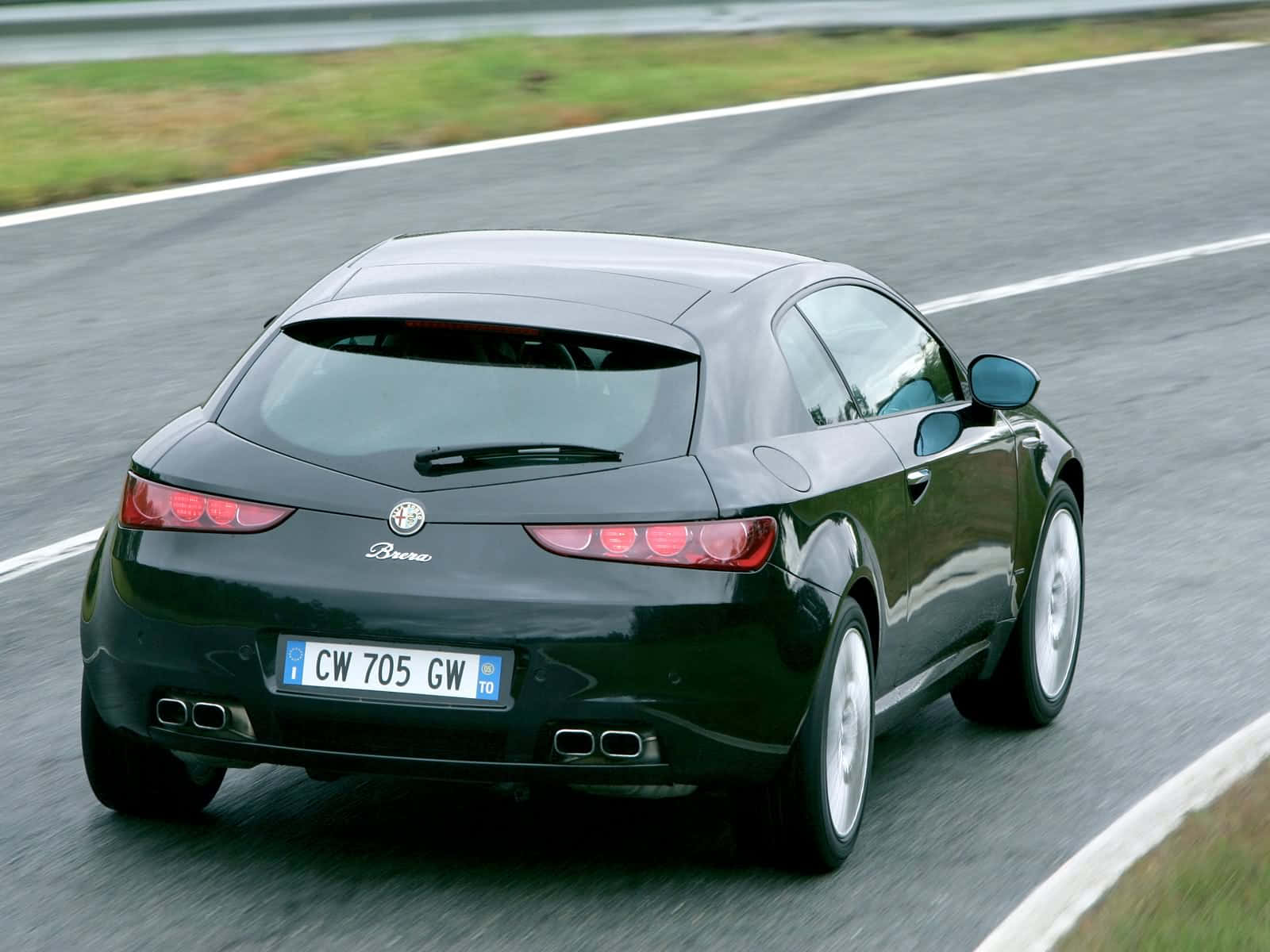 Alfa Romeo Brera 桌布 壁紙 — 一輛流線型的黑色愛快羅密歐 Brera 跑車在濕滑的瀝青路上飛馳，路旁有模糊的綠色草地和白色行車線。