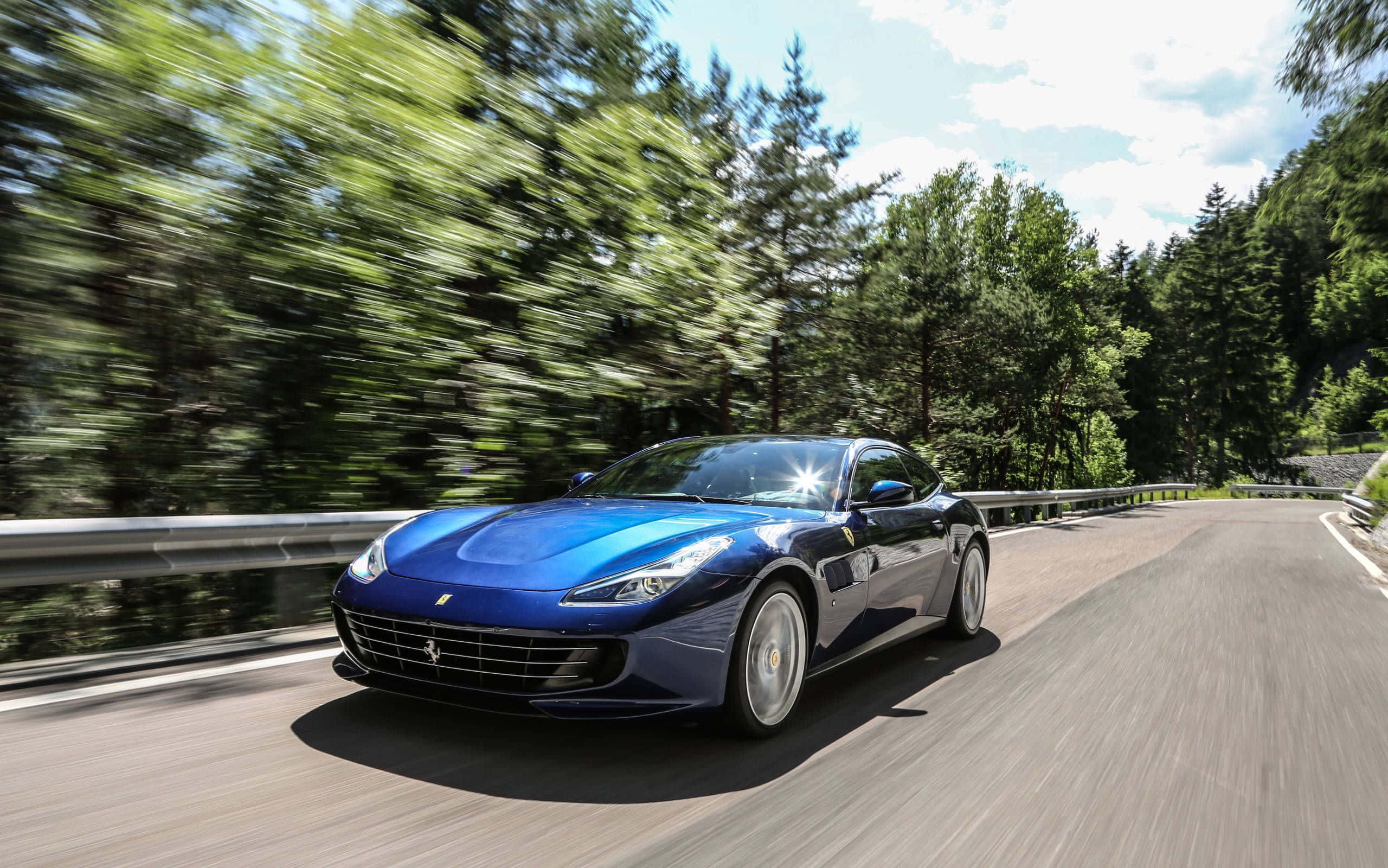Ferrari Gtc4lusso 桌布 壁紙 — 一輛流線型藍色法拉利在蜿蜒的森林道路上疾馳，周圍帶有動態模糊效果。