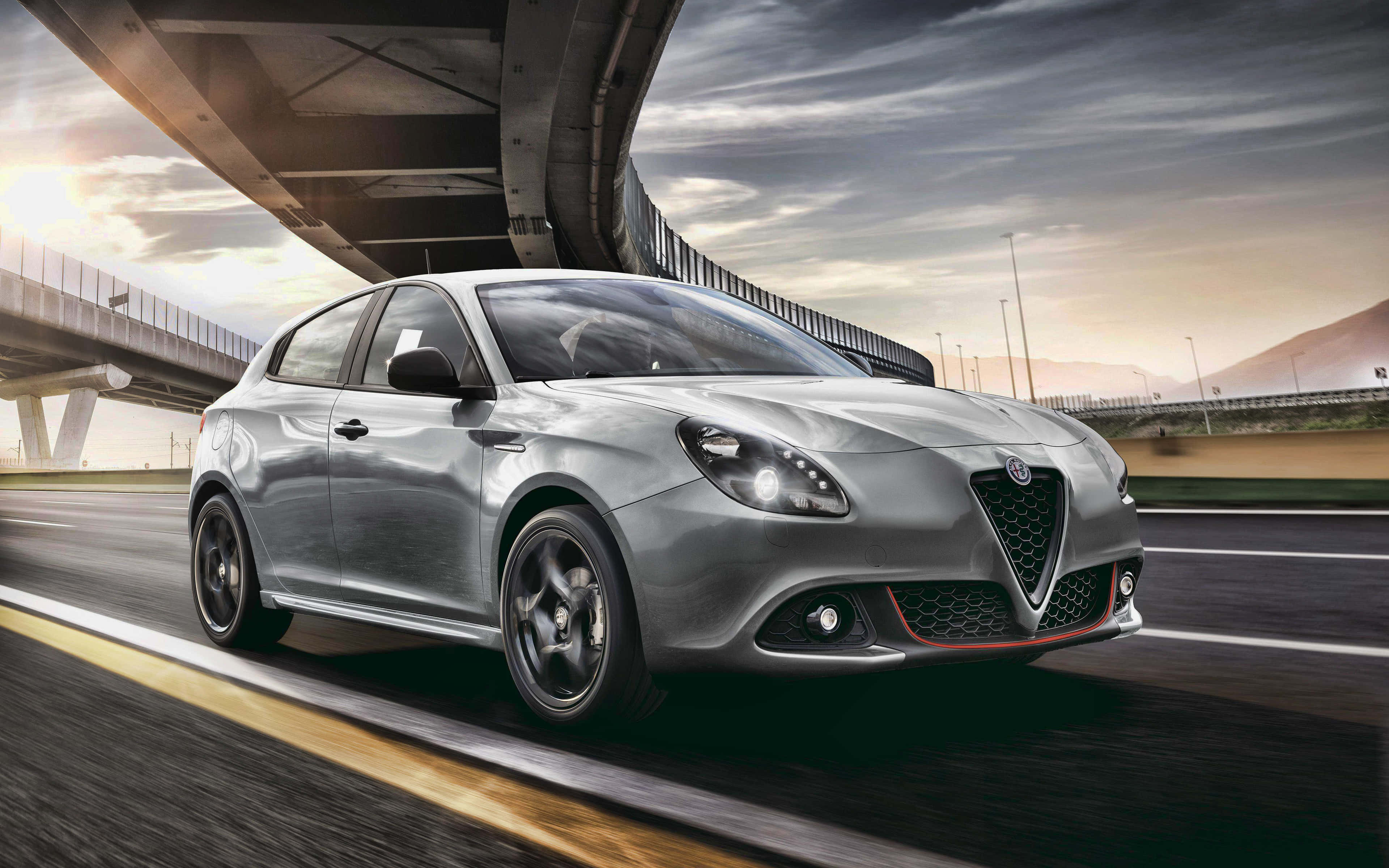 Alfa Romeo Giulietta 桌布 壁紙 — 一輛流線型銀色愛快羅密歐跑車在黃金時段於混凝土天橋下行駛，路上帶有動態模糊效果。