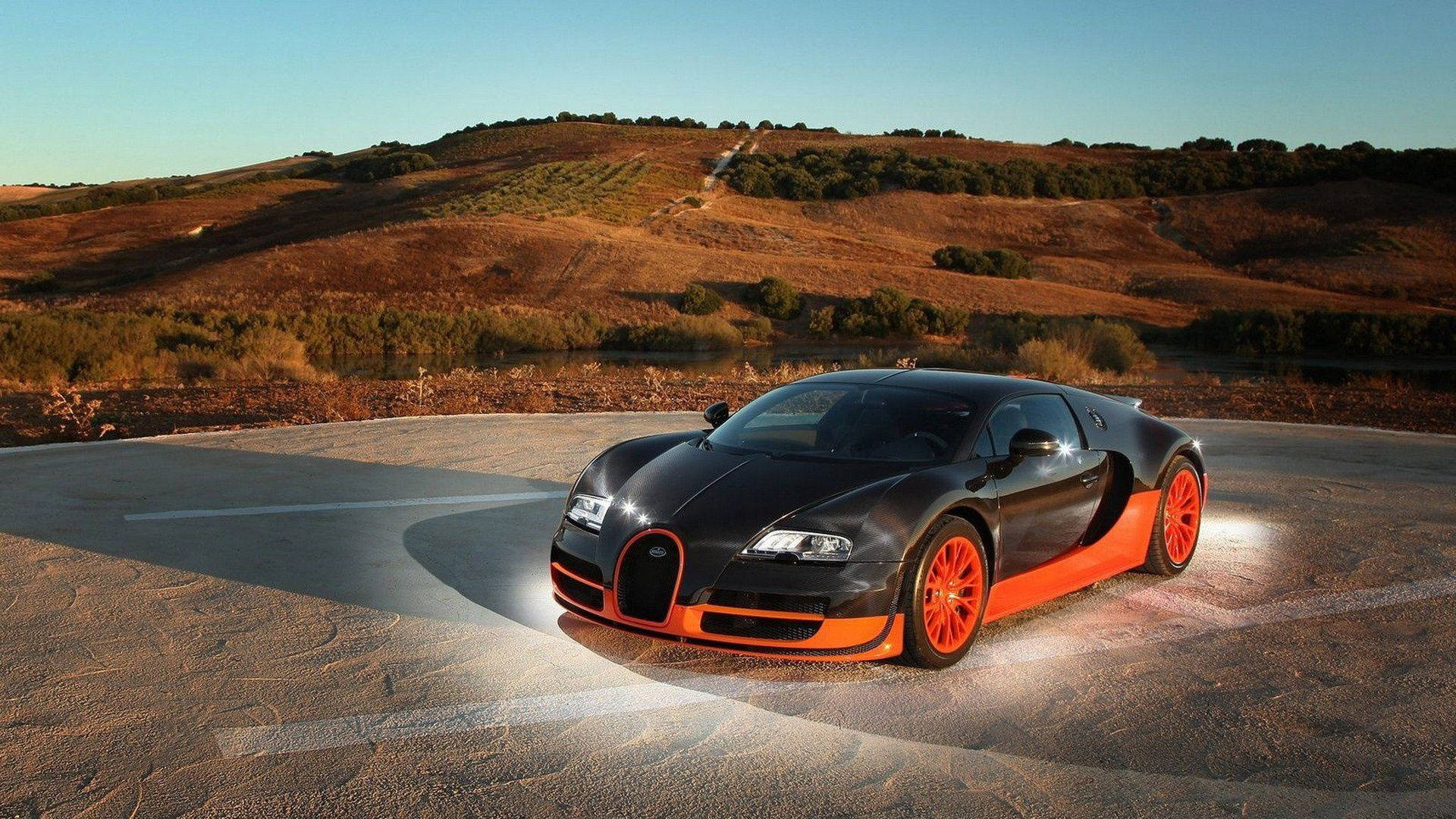 HD 桌布 壁紙 — 一輛流線型黑橙色Bugatti Veyron在彎曲道路上閃耀，沐浴在金色夕陽光下，背景是起伏的丘陵。