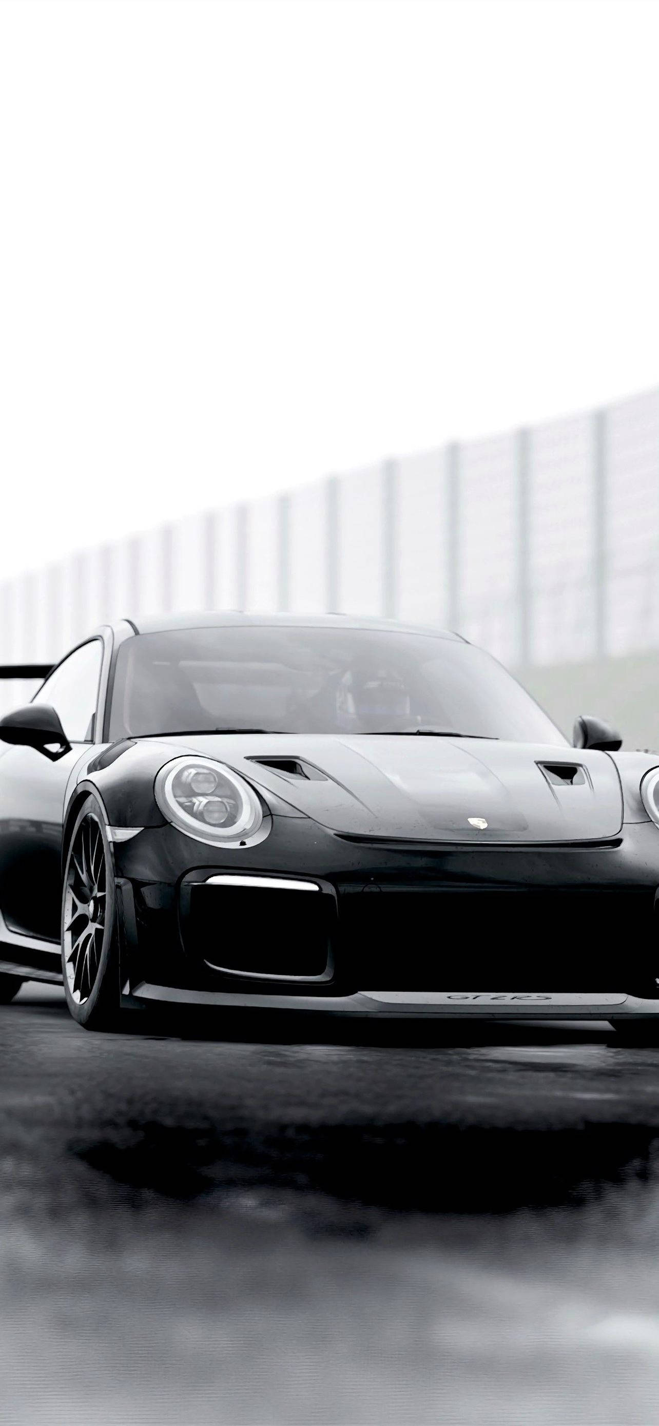 保時捷 桌布 壁紙 — 一輛流線型黑色保時捷911 GT2 RS在賽道上，背景是模糊的動感和霧氣瀰漫的瀝青路面，天空多雲。