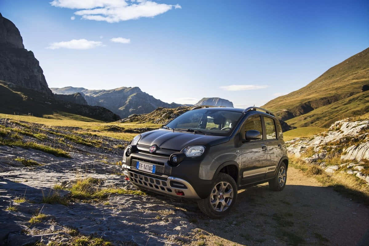 Fiat Panda 桌布 壁紙 — 一輛深灰色嘅Fiat Panda Cross停喺岩石山徑上，頭頂係晴朗藍天同零星白雲。