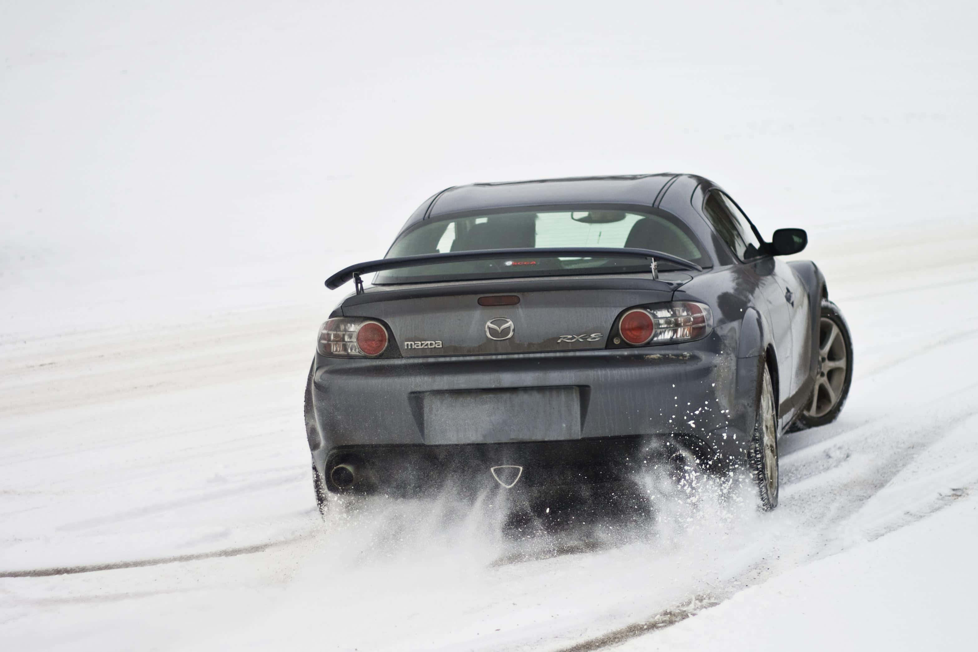 Mazda Rx-8 桌布 壁紙 — 一輛深灰色萬事得RX-8跑車在雪景中行駛時揚起雪花。