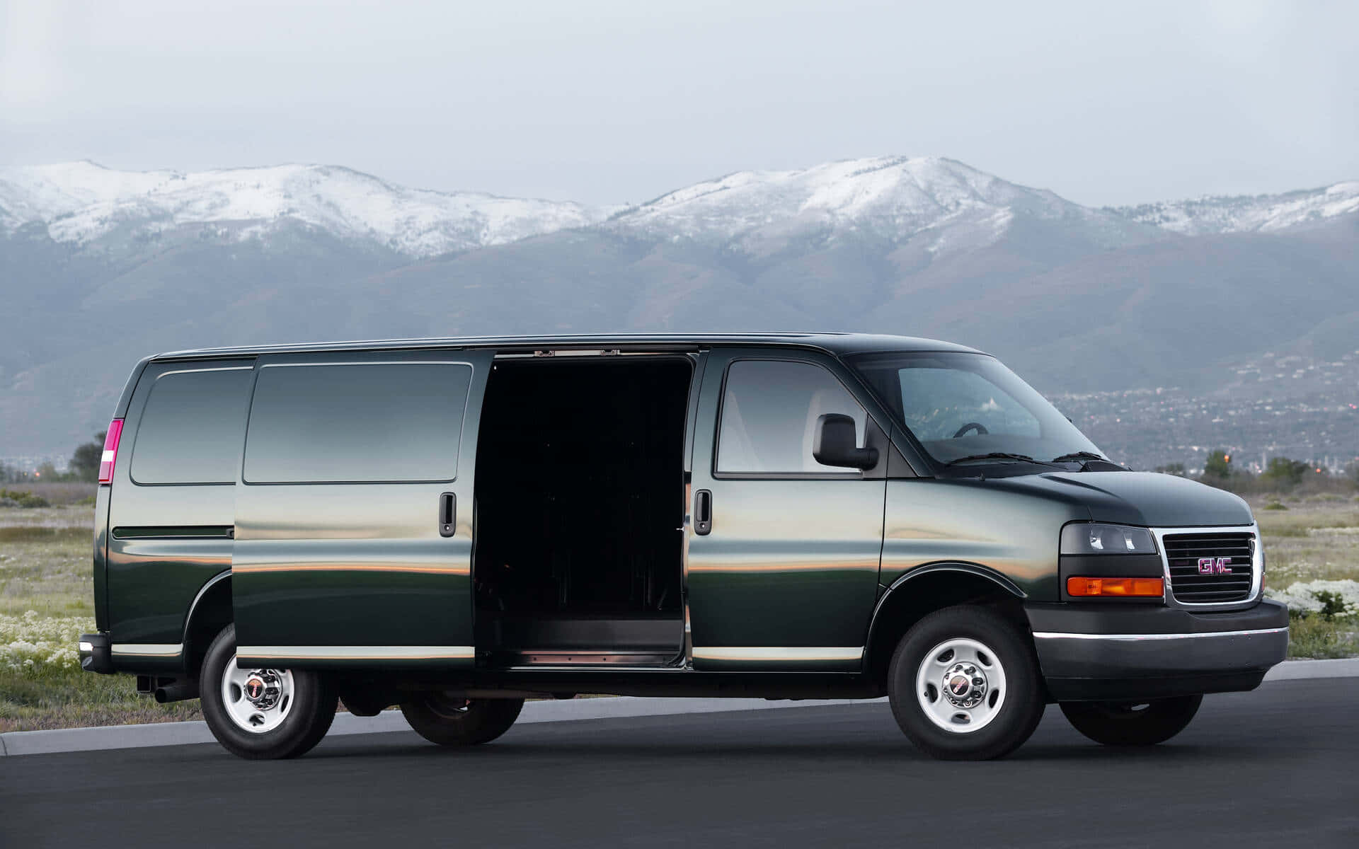 Gmc Savana 桌布 壁紙 — 一輛深綠色GMC客貨車側門打開，停在路上，背景是白雪覆蓋的山脈。