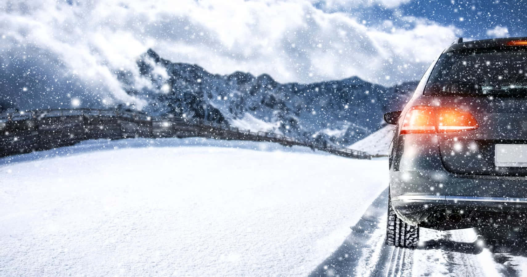 Winter Driving 桌布 壁紙 — 一輛深色SUV駛過積雪的山口，雪花在陰雲密布的天空中飄落。