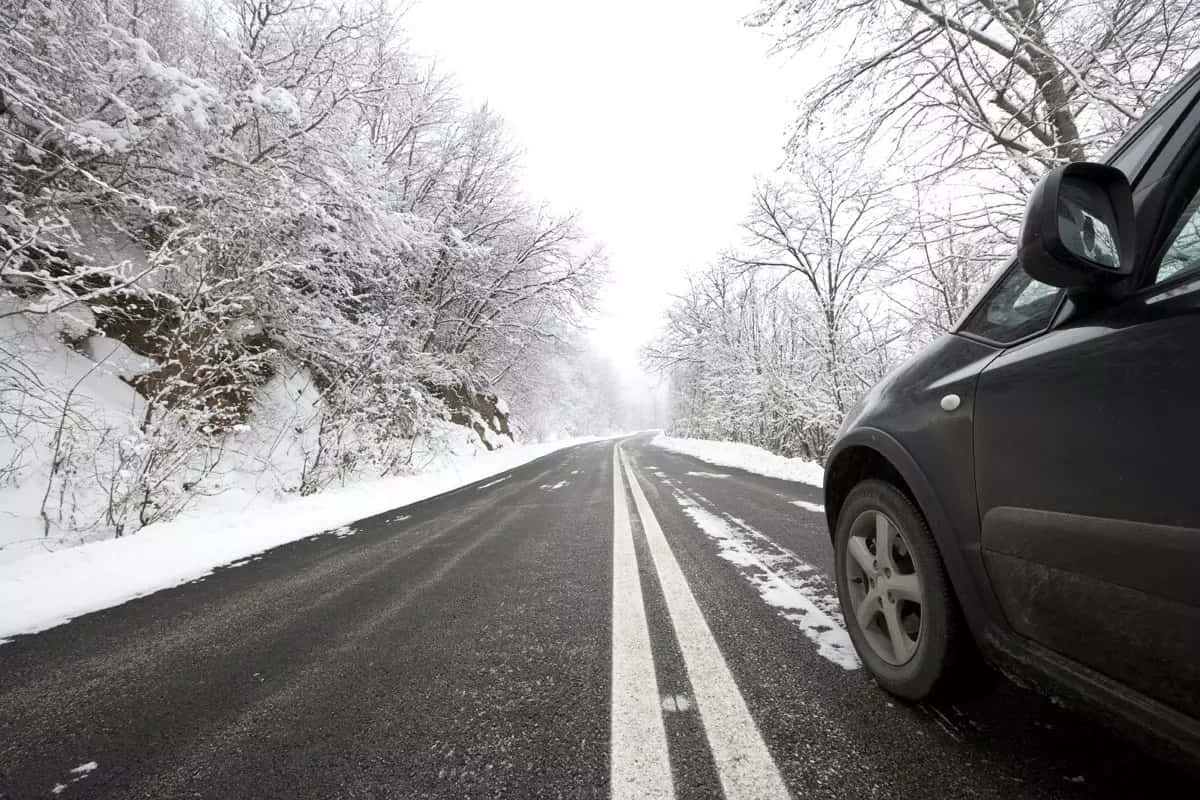 Winter Driving 桌布 壁紙 — 一輛深色汽車停泊在積雪的道路上，兩旁是結霜的樹木，天空是陰沉的冬日天空。