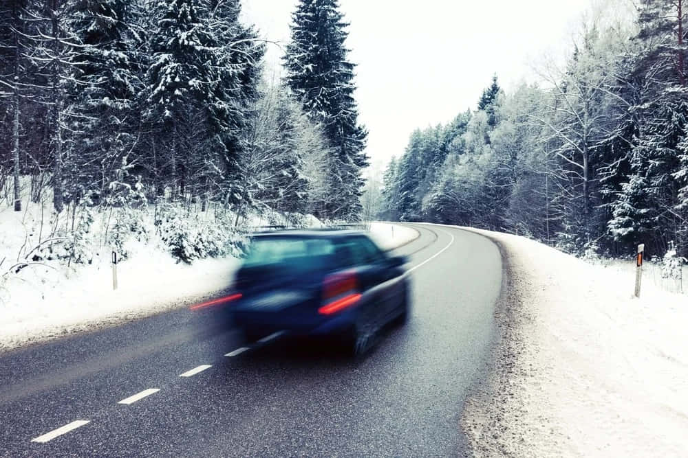 Winter Driving 桌布 壁紙 — 一輛深色汽車在白雪覆蓋的松樹林間道路上模糊地行駛，天空多雲。