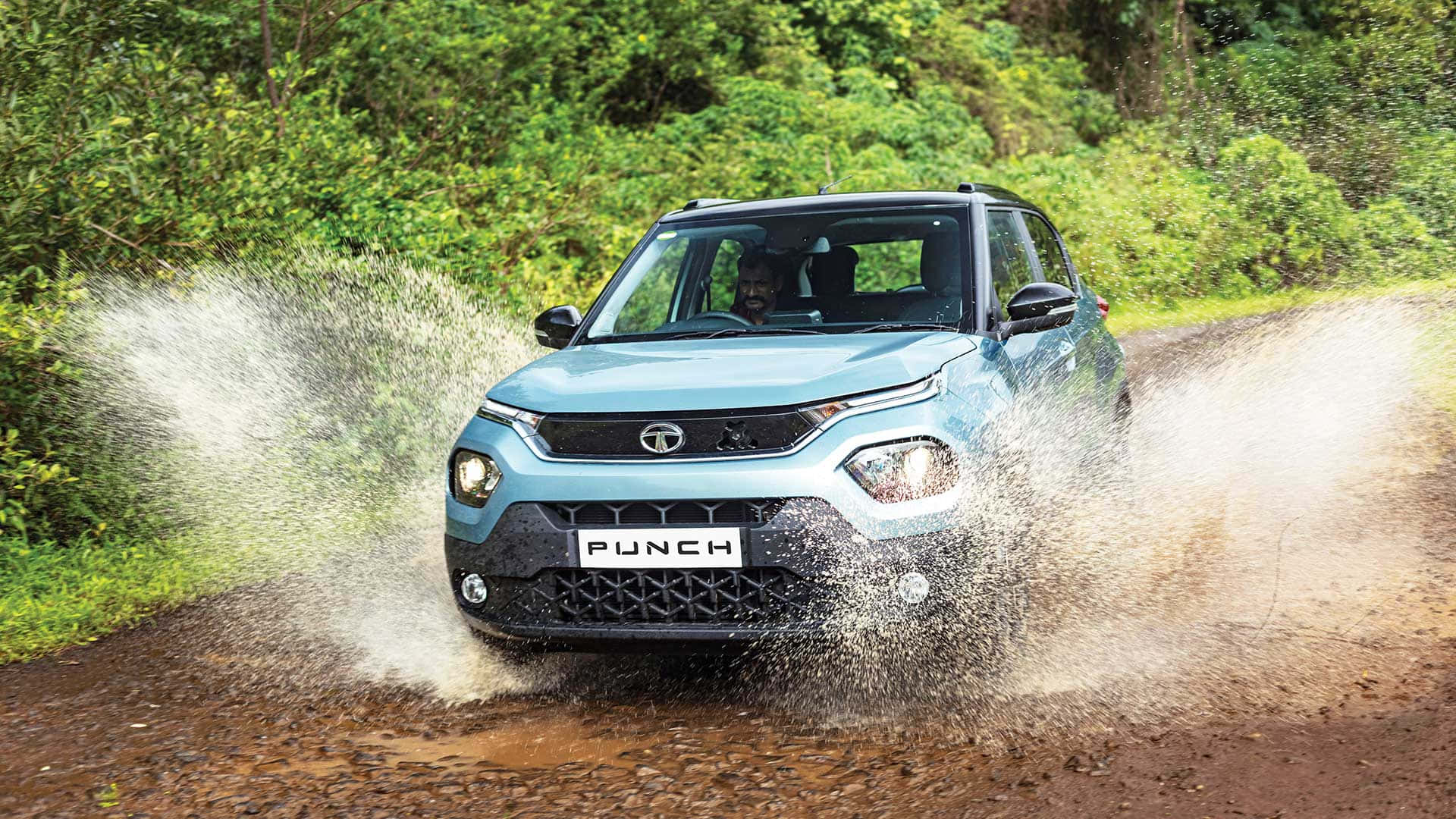 Tata Motors 桌布 壁紙 — 一輛淺藍色的Tata Punch SUV在森林道路上濺起泥濘水花，背景是綠色樹葉。