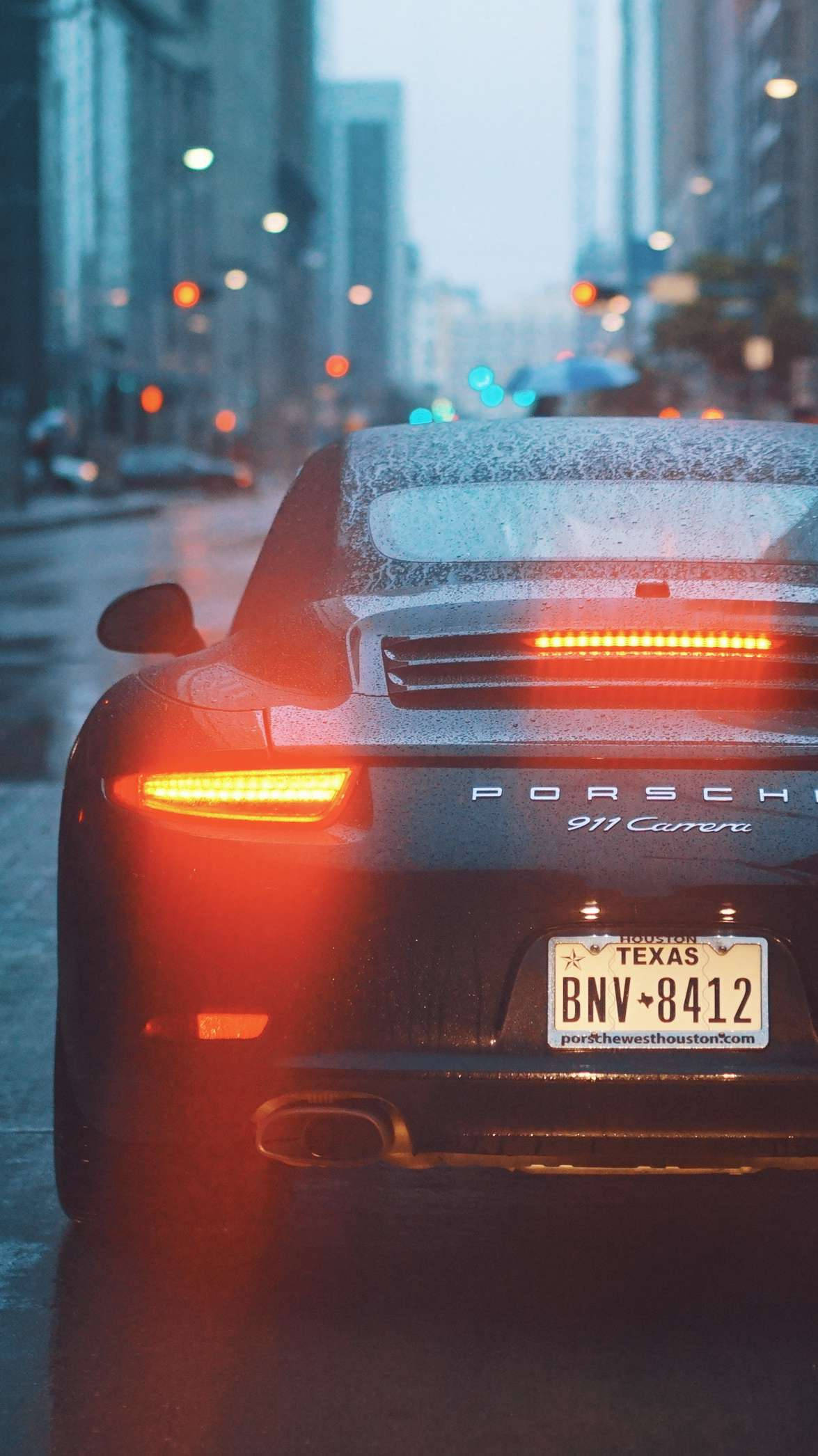 Sports Car 桌布 壁紙 — 一輛濕透的黑色保時捷911 Carrera，在黃昏時分的雨城市街道上停泊，紅色尾燈閃爍發光。