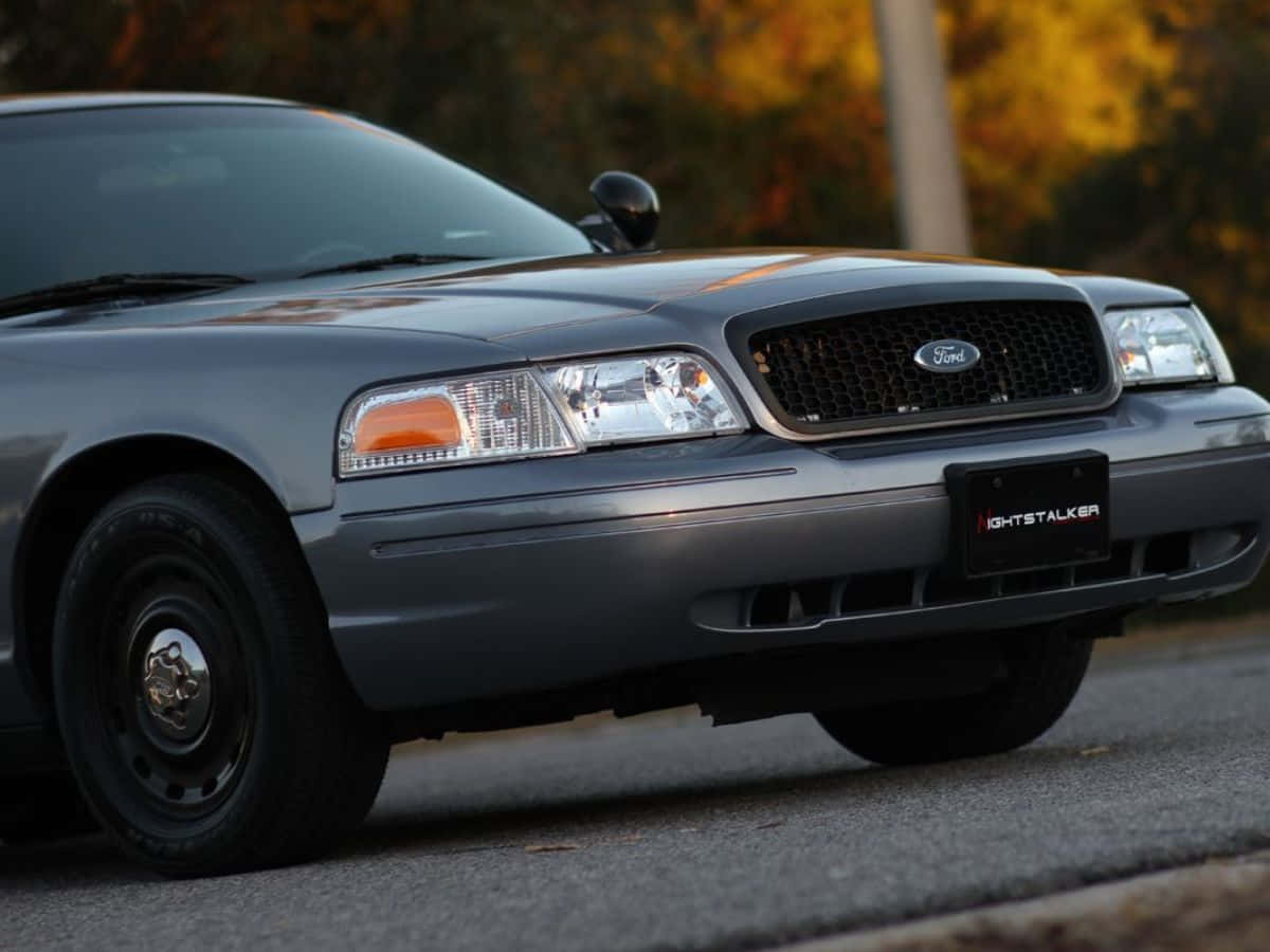 Ford Crown Victoria 桌布 壁紙 — 一輛灰色福特皇冠維多利亞警車停在瀝青路上，身後秋樹在溫暖光線中閃耀。