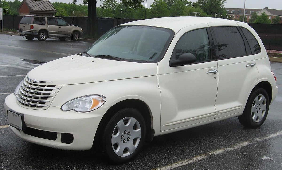 Chrysler Pt Cruiser 桌布 壁紙 — 一輛白色 Chrysler PT Cruiser 停泊在濕漉漉的瀝青停車場，背景有樹木和圍欄。