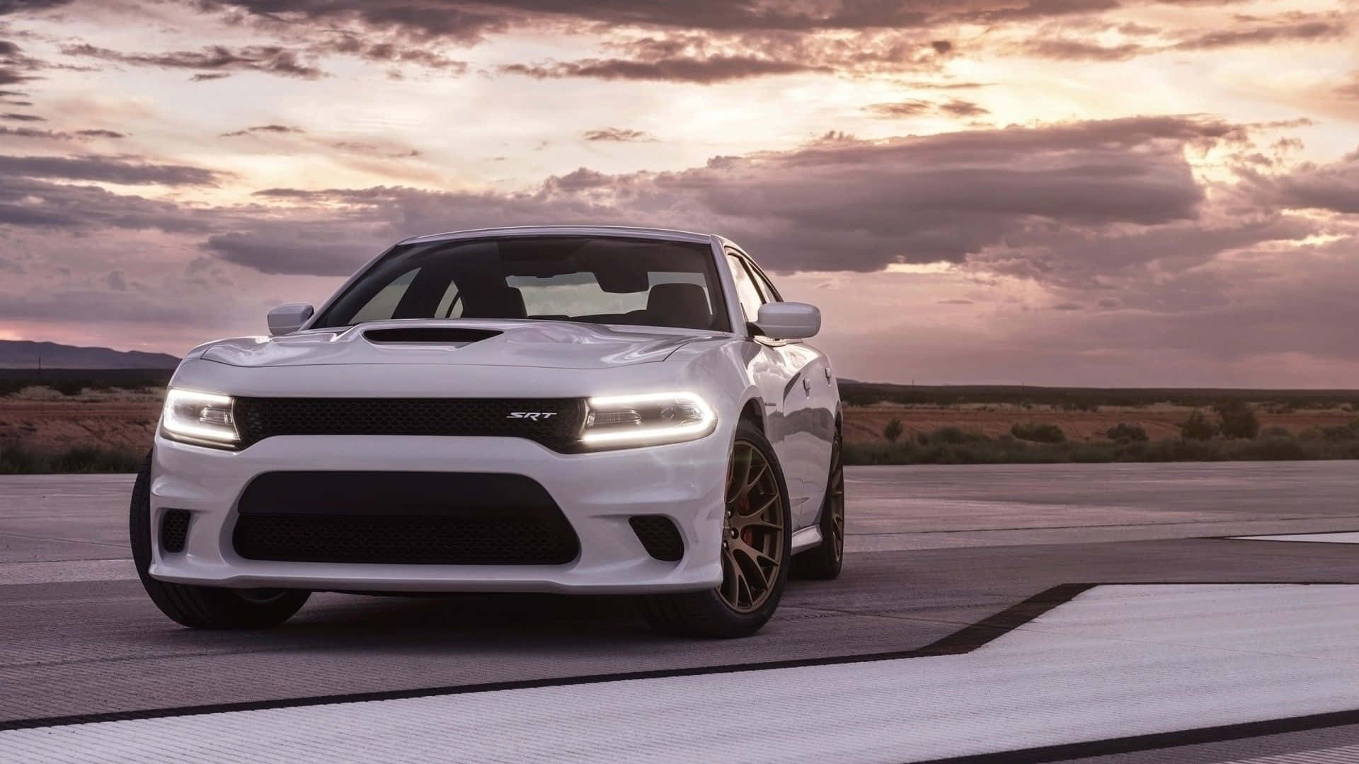 Dodge Charger 桌布 壁紙 — 一輛白色 Dodge Charger SRT 在沙漠賽道上，於夕陽西下、雲彩染上溫暖色調的戲劇性天空下閃耀。