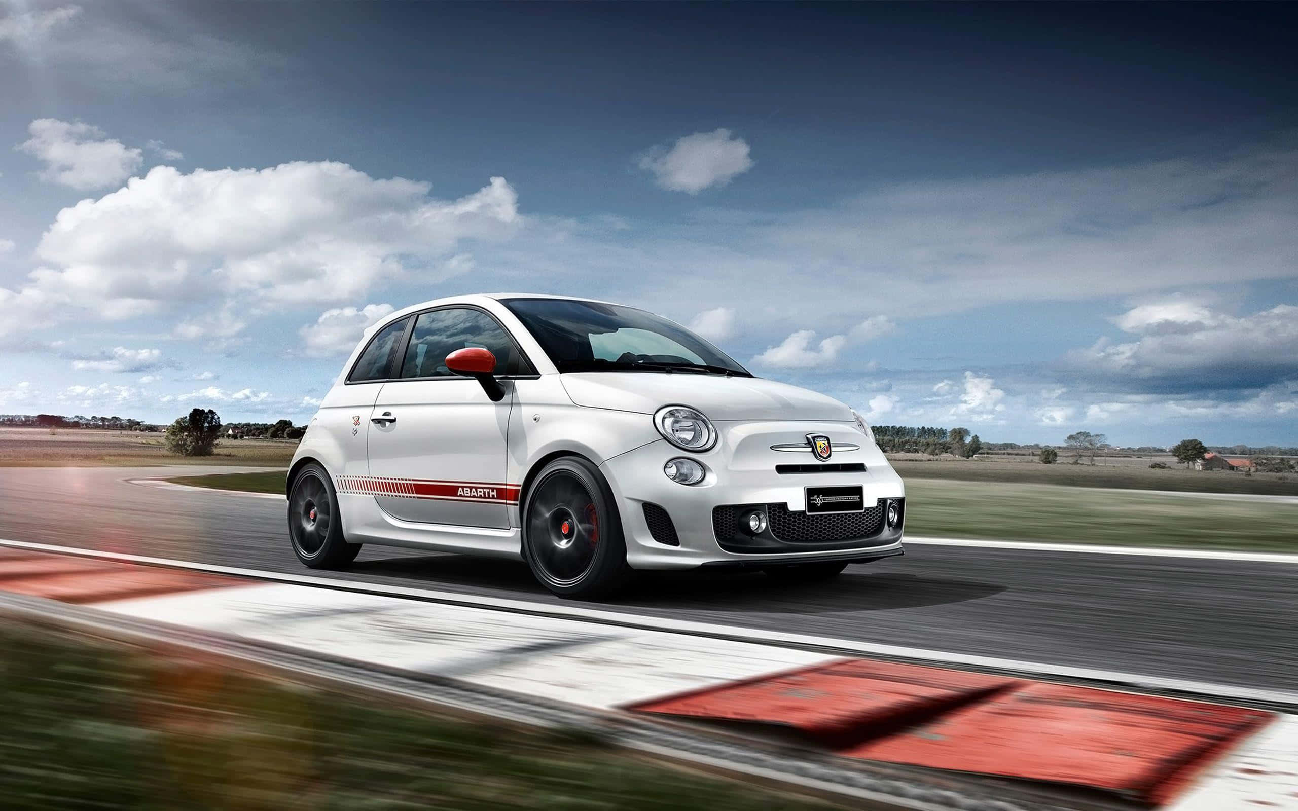 Abarth 桌布 壁紙 — 一輛白色 Fiat Abarth 在戲劇性的多雲天空下，以模糊動態效果在賽道上疾馳。