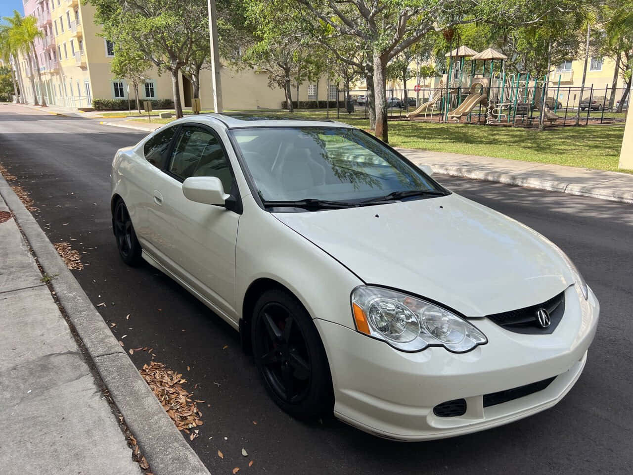 Acura Rsx 桌布 壁紙 — 一輛白色Acura TSX雙門轎跑車，配黑色輪圈，停在遊樂場附近的林蔭街道上。