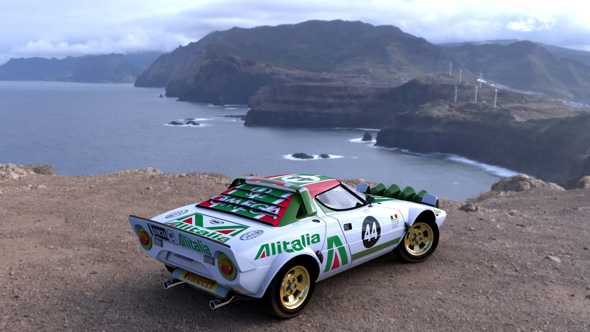 Lancia 桌布 壁紙 — 一輛白色Alitalia拉力賽車配金色輪圈，停泊在懸崖上，俯瞰崎嶇的海岸灣，遠山上有風力發電機。