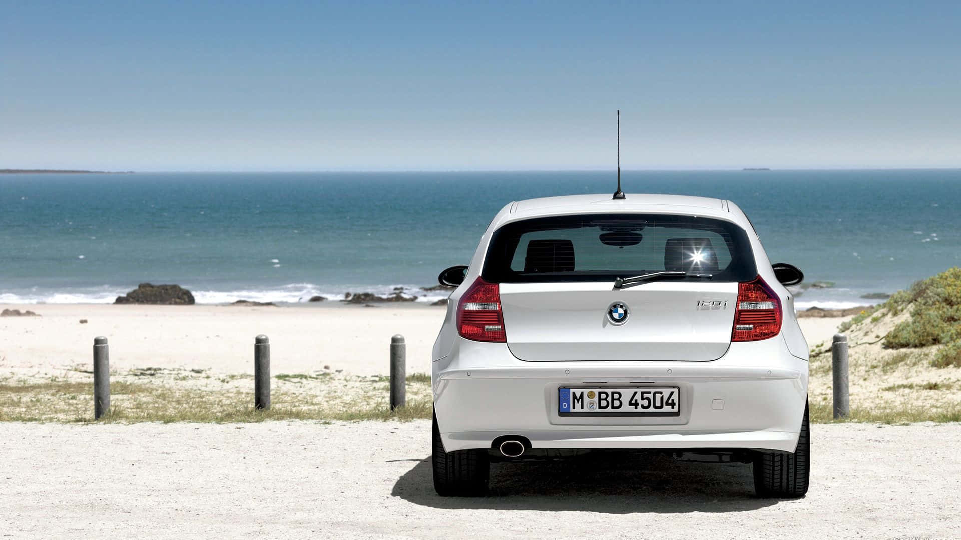 Bmw 1 Series 桌布 壁紙 — 一輛白色BMW 1系停泊在碎石路上，面向晴朗天空下廣闊的藍色海洋。