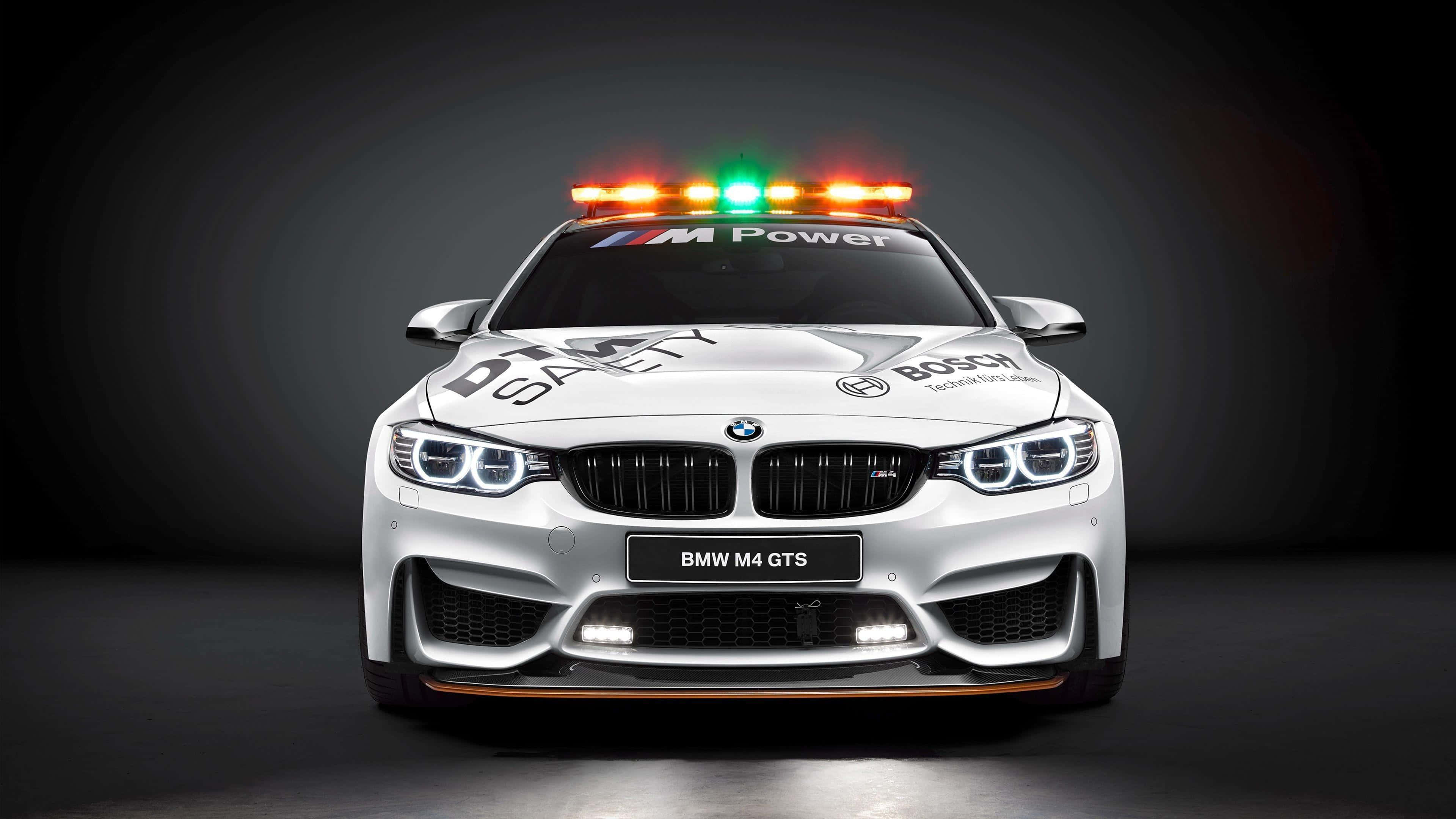 Safety Car 桌布 壁紙 — 一輛白色BMW M4 GTS賽車，配備安全燈和贊助商貼紙，正面朝向深色工作室背景。